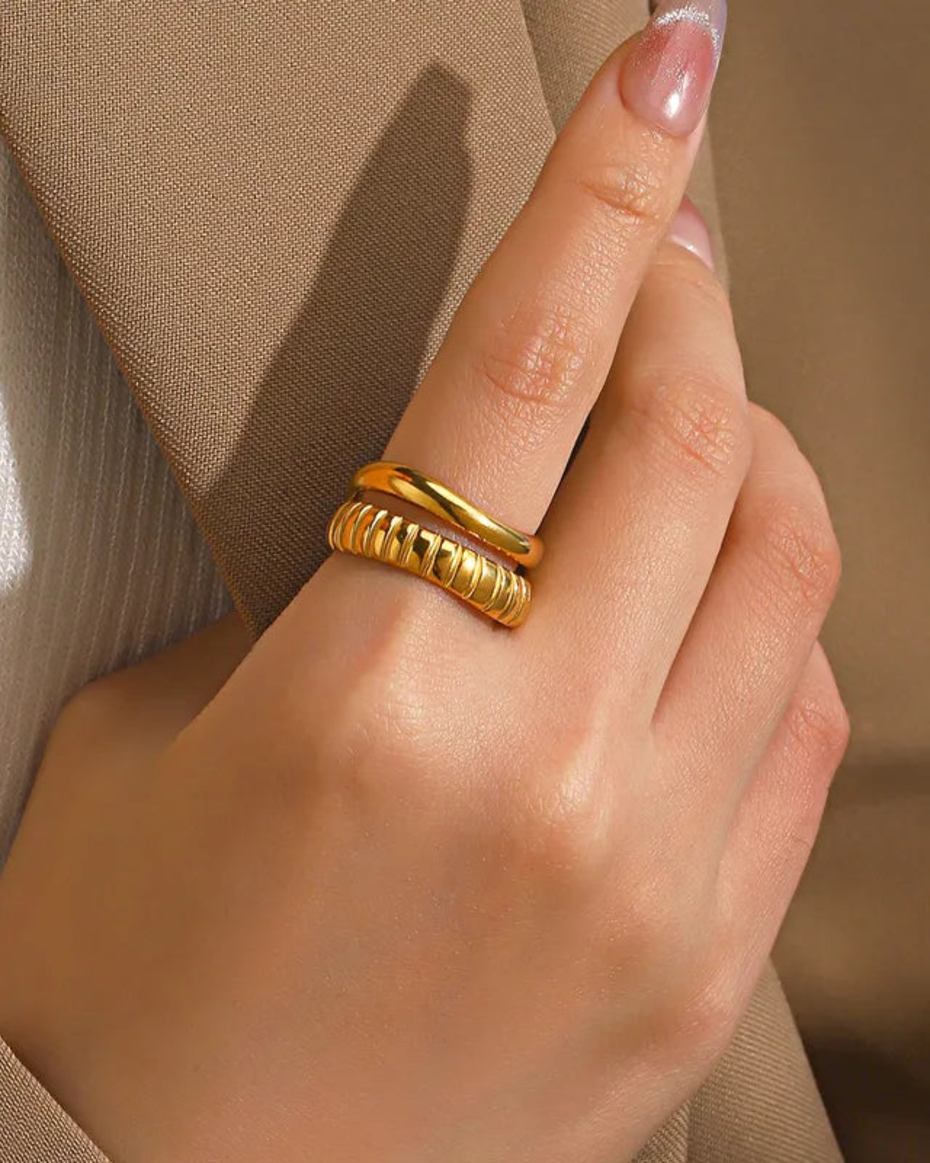Hand wearing a gold ring with a blurred beige background