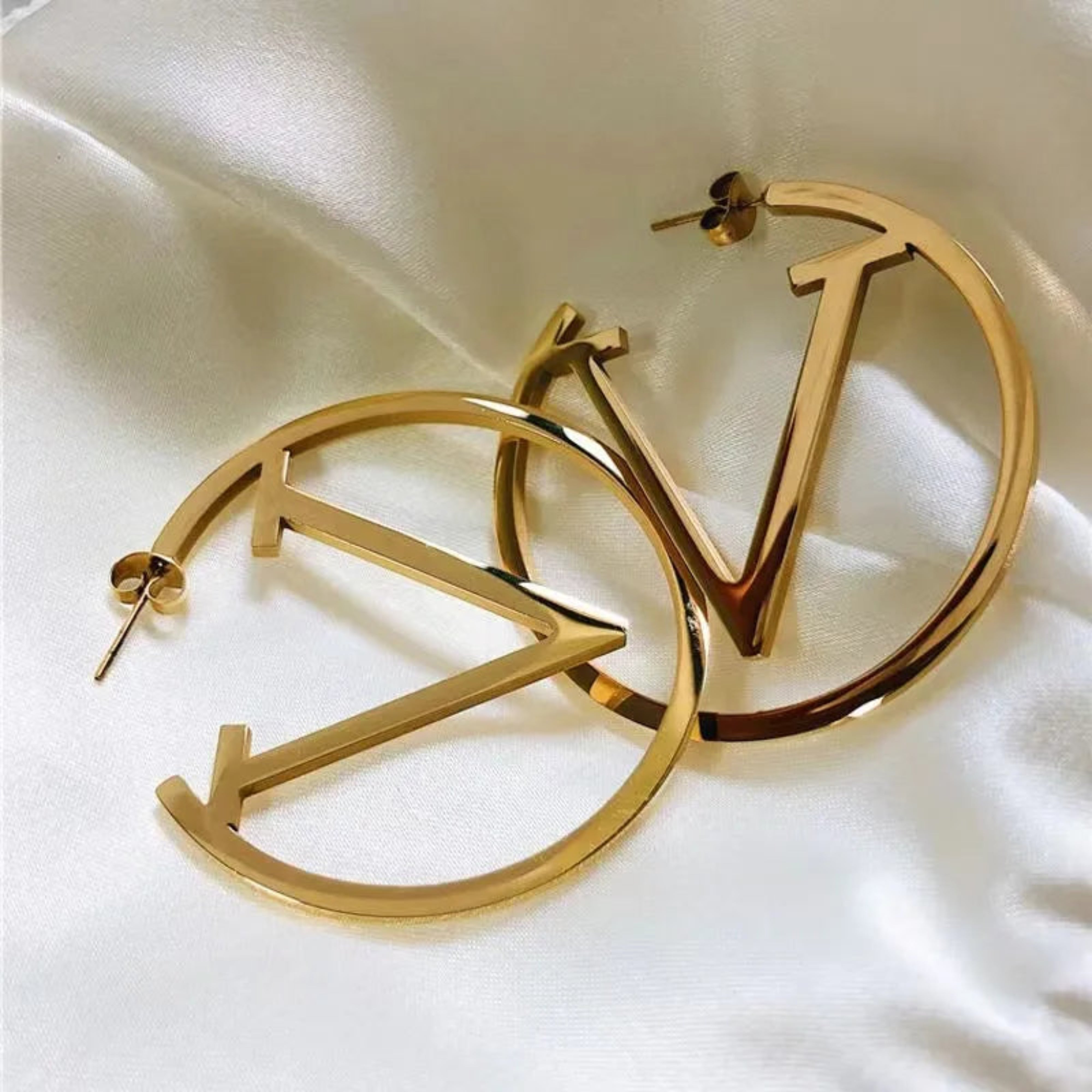 Gold hoop earrings with a logo on a white fabric background