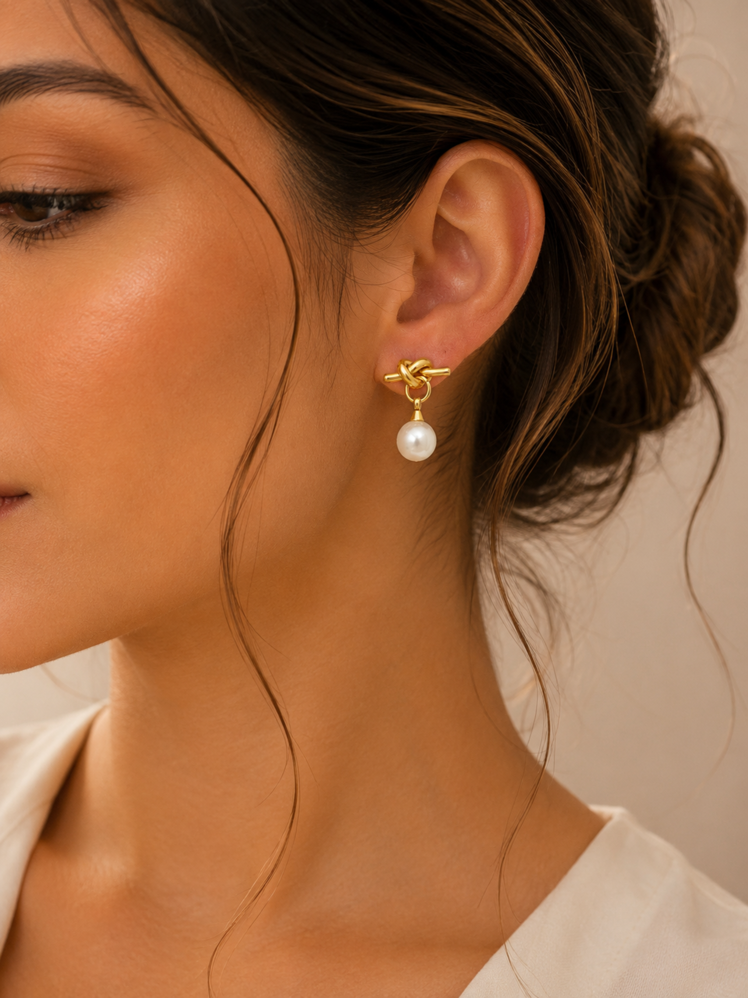 Close-up of a woman wearing a gold earring with a pearl on a neutral background