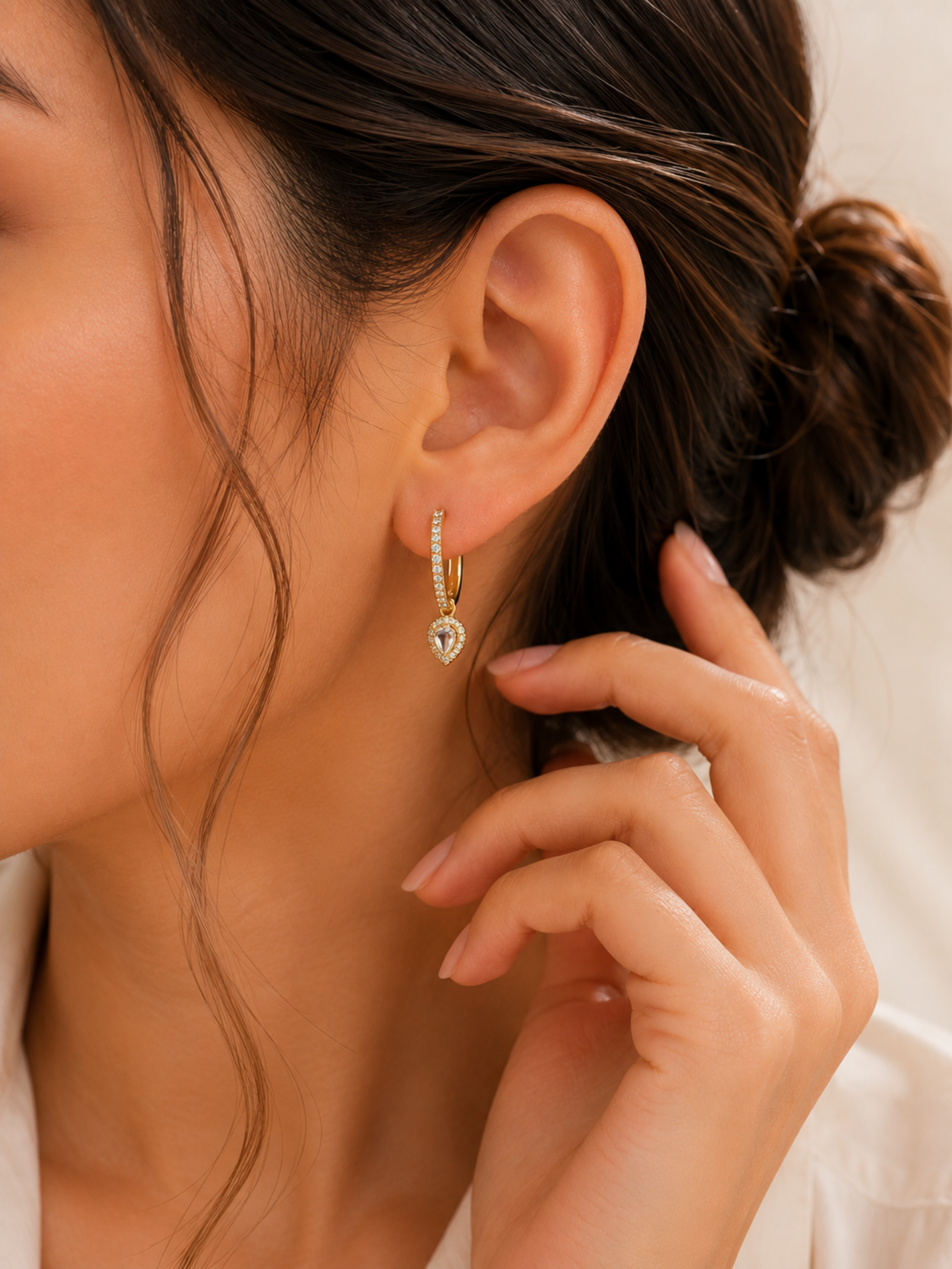 Close-up of a woman wearing a gold earring with a heart-shaped gemstone.