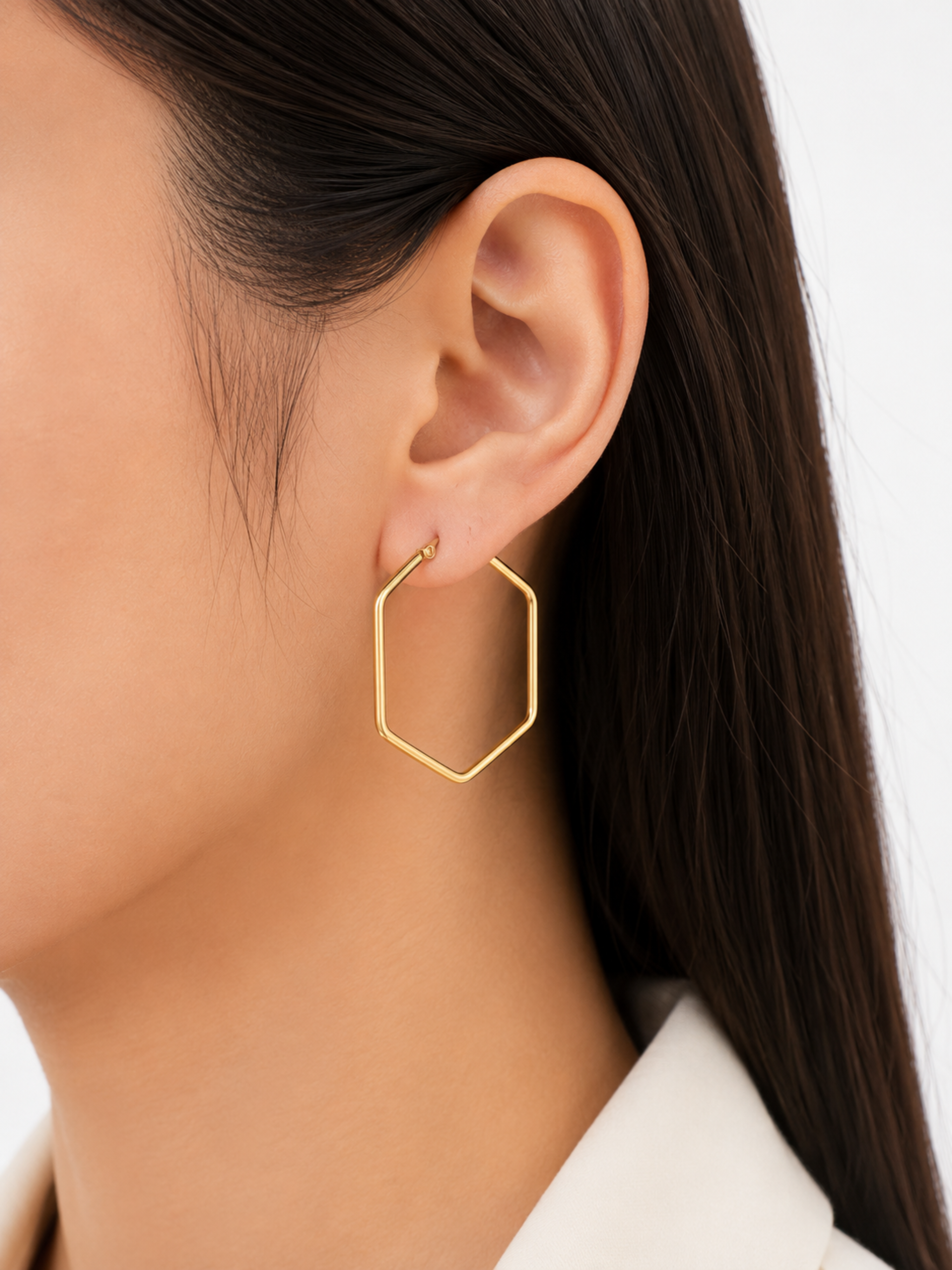 Gold hexagonal hoop earring worn by a person with long dark hair.