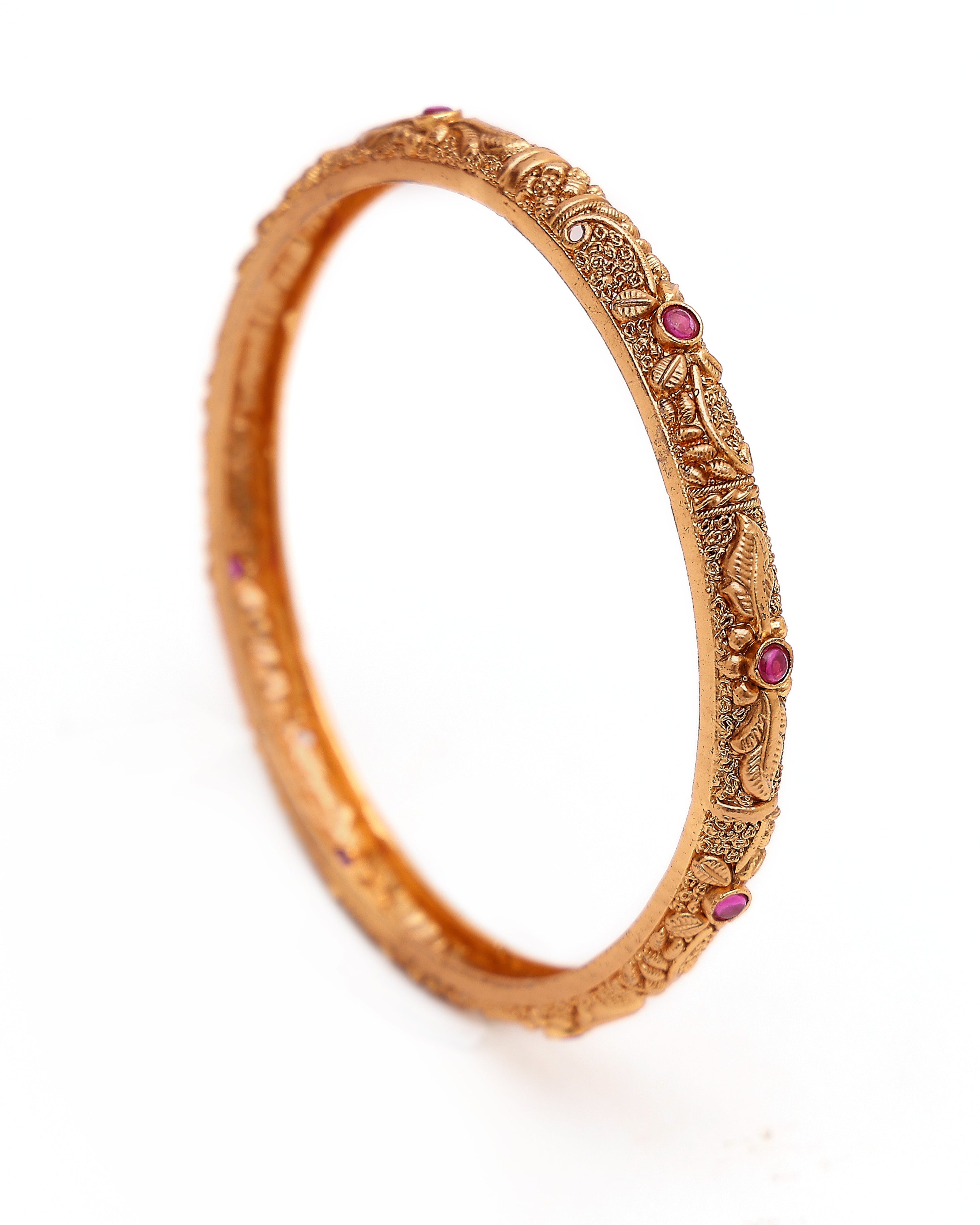 Gold bracelet with intricate designs and red stones on a white background