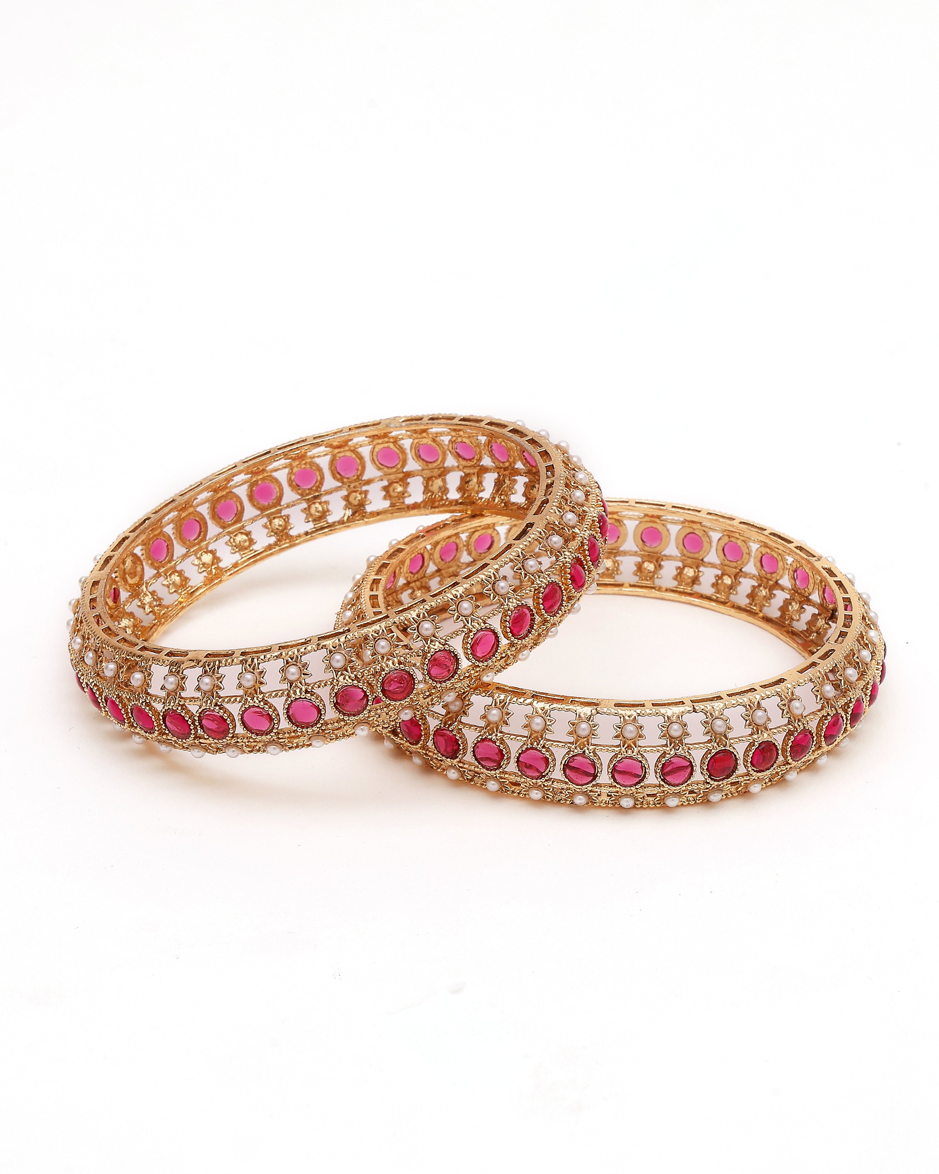 Pair of gold bangles with pink stones on a white background