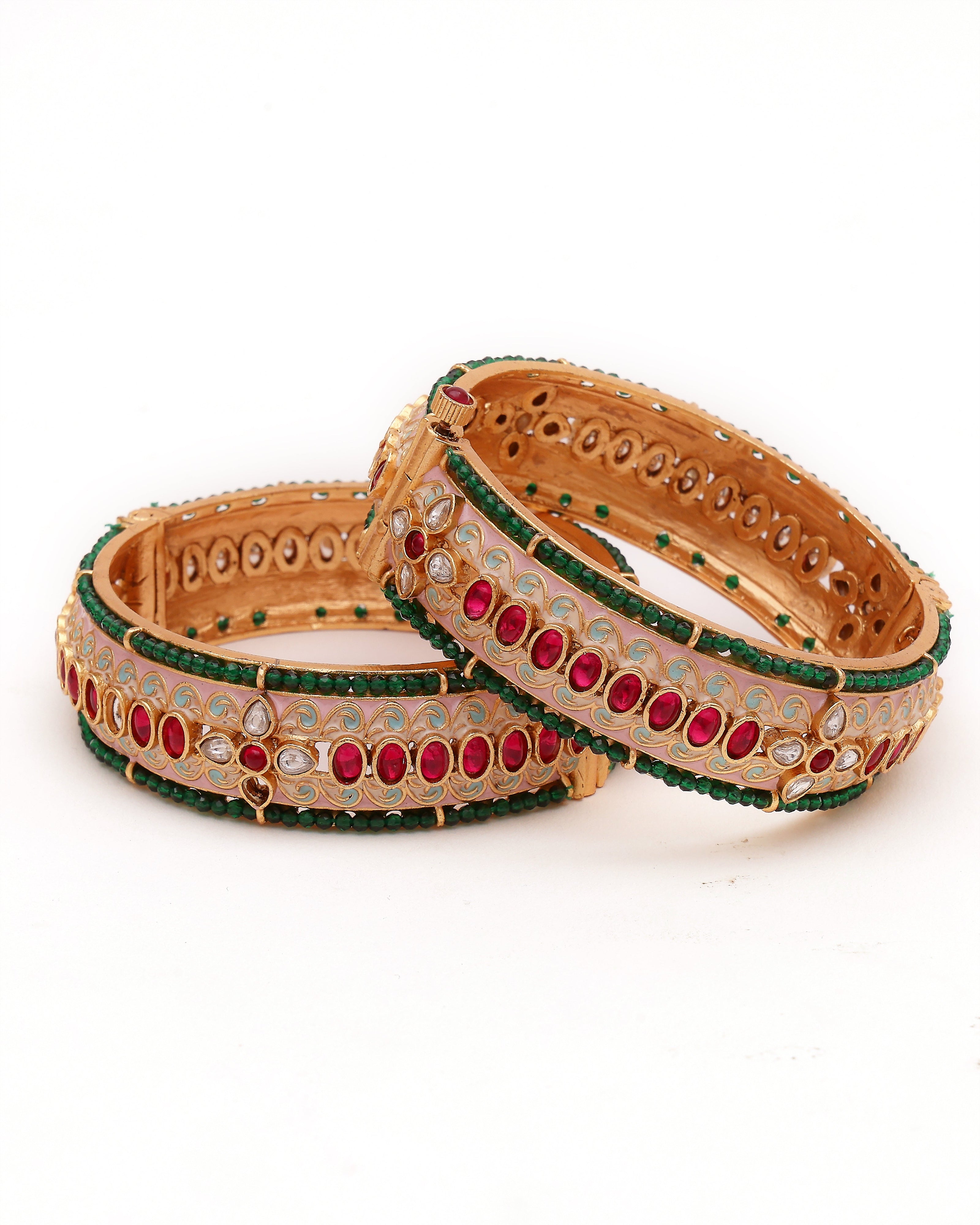 Pair of ornate gold bangles with red and green stones on a white background