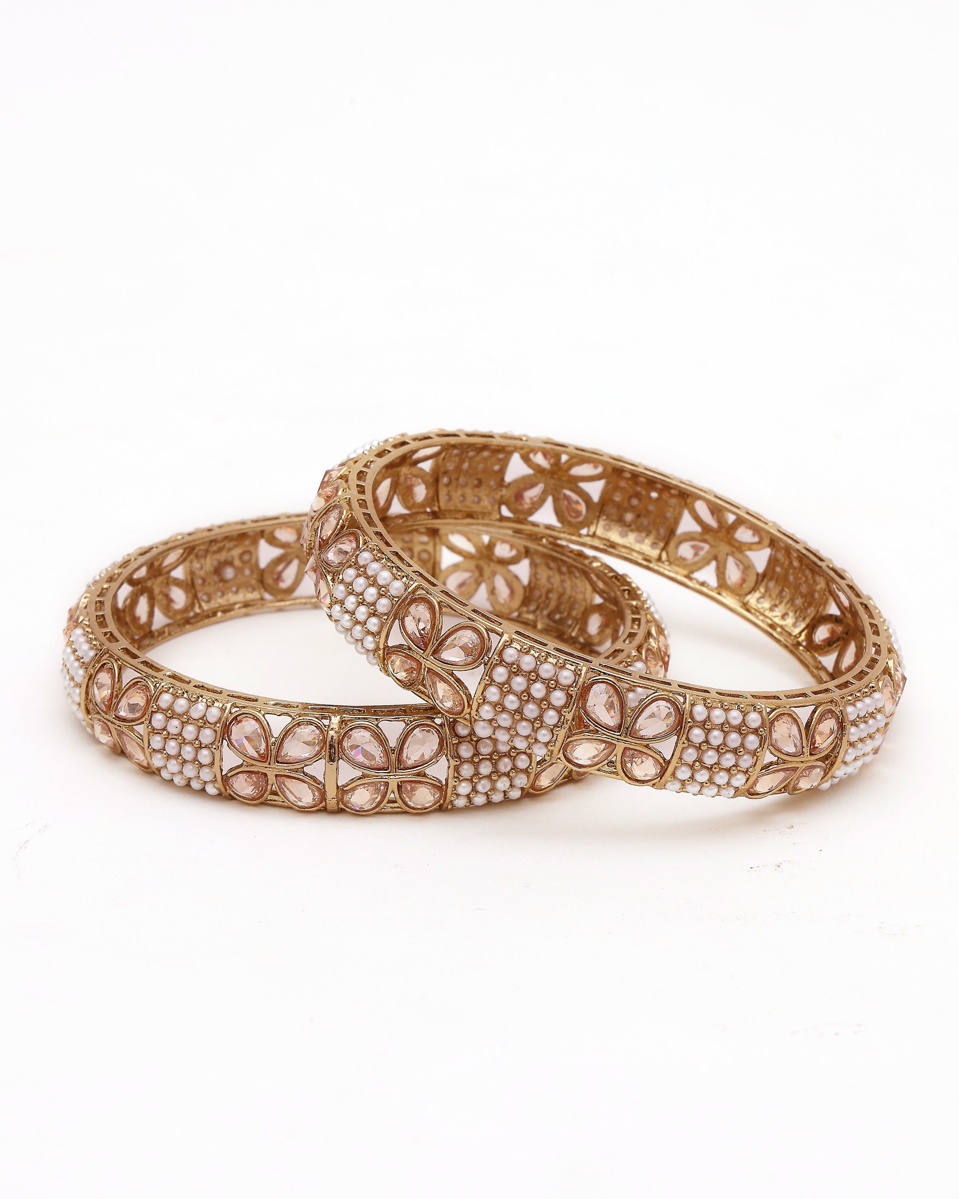 Pair of gold bangles with intricate designs on a white background