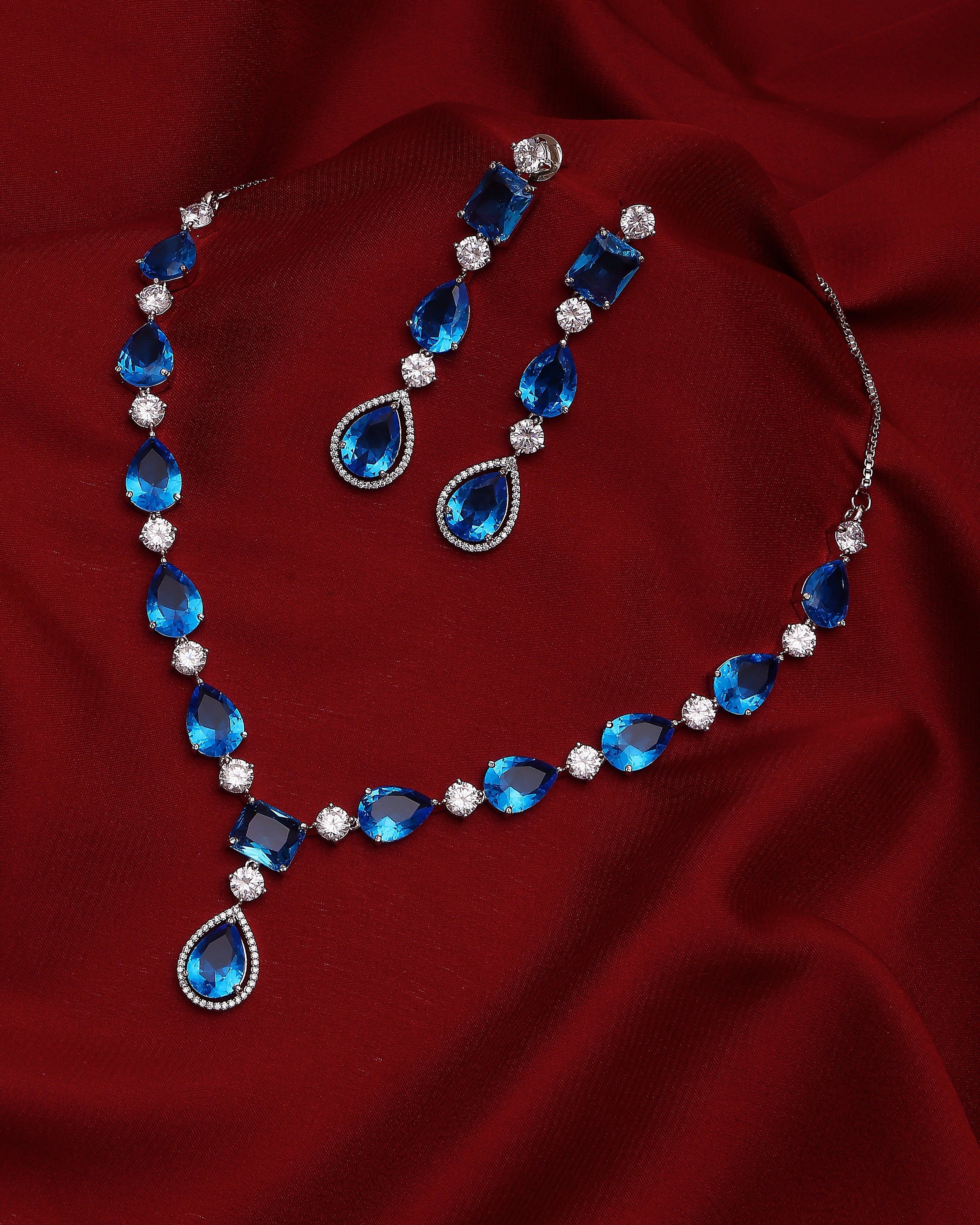 Blue teardrop necklace and earrings on a red fabric background