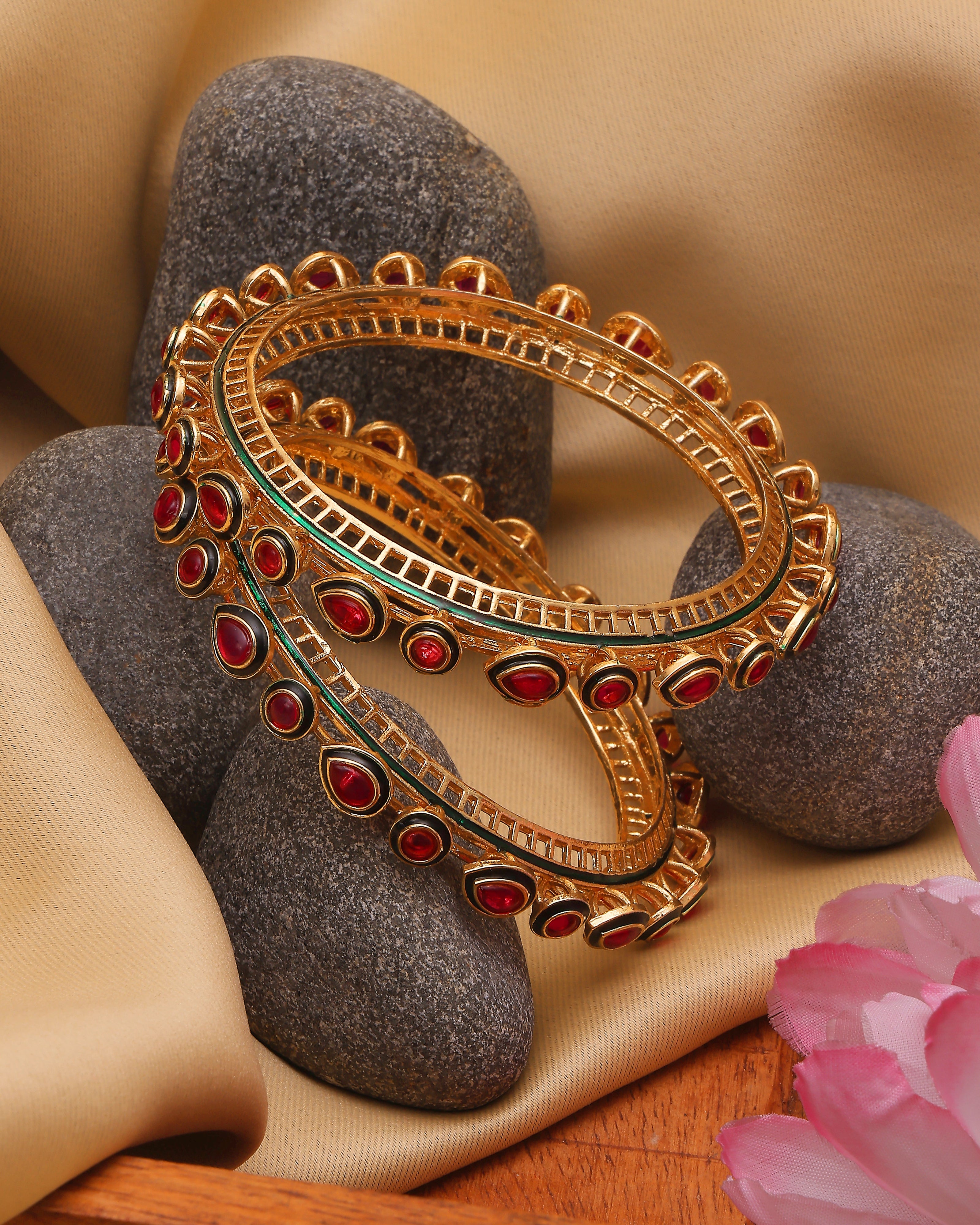 Gold bangles with red stones on a stone surface with pink flowers