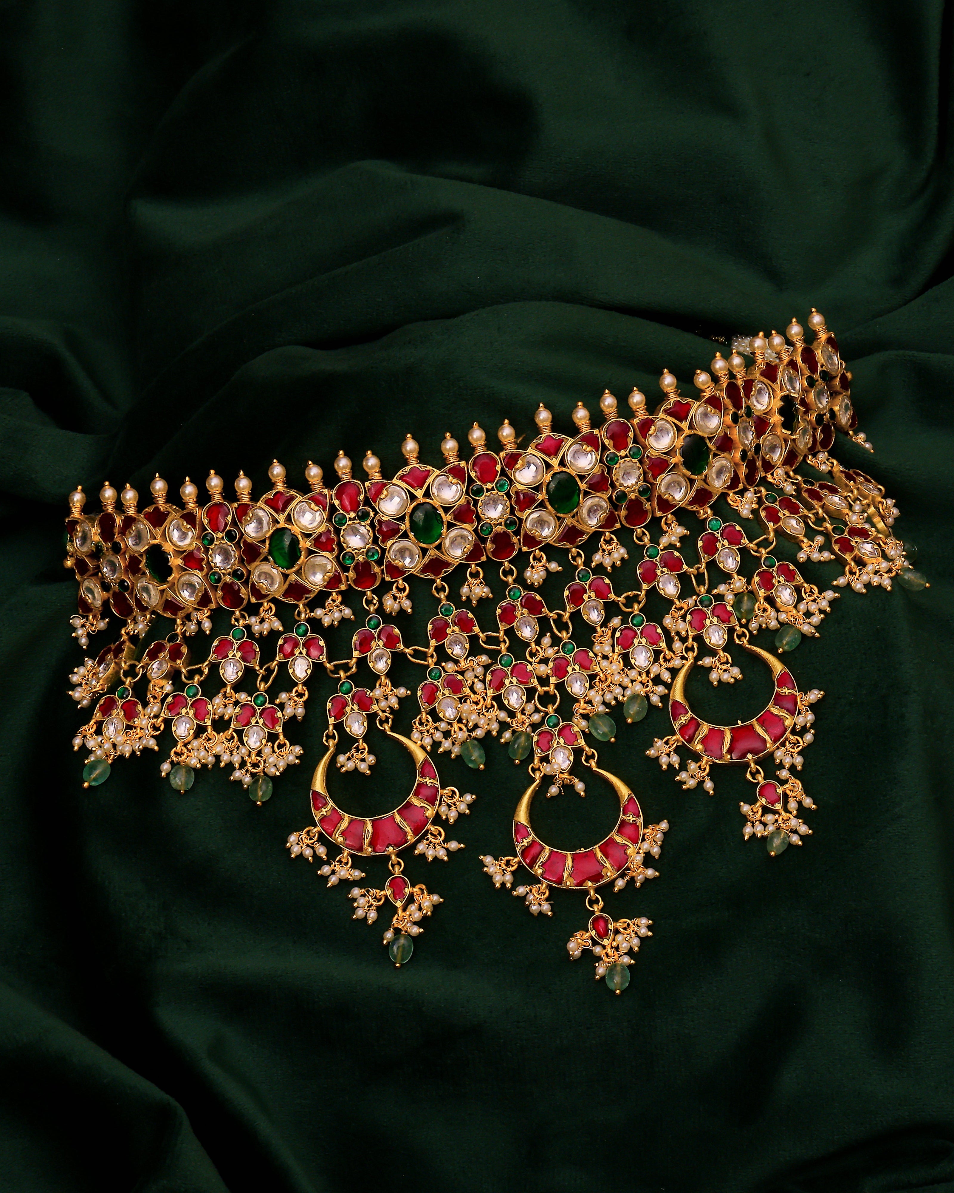 Ornate gold necklace with red and green gemstones on a dark green fabric background