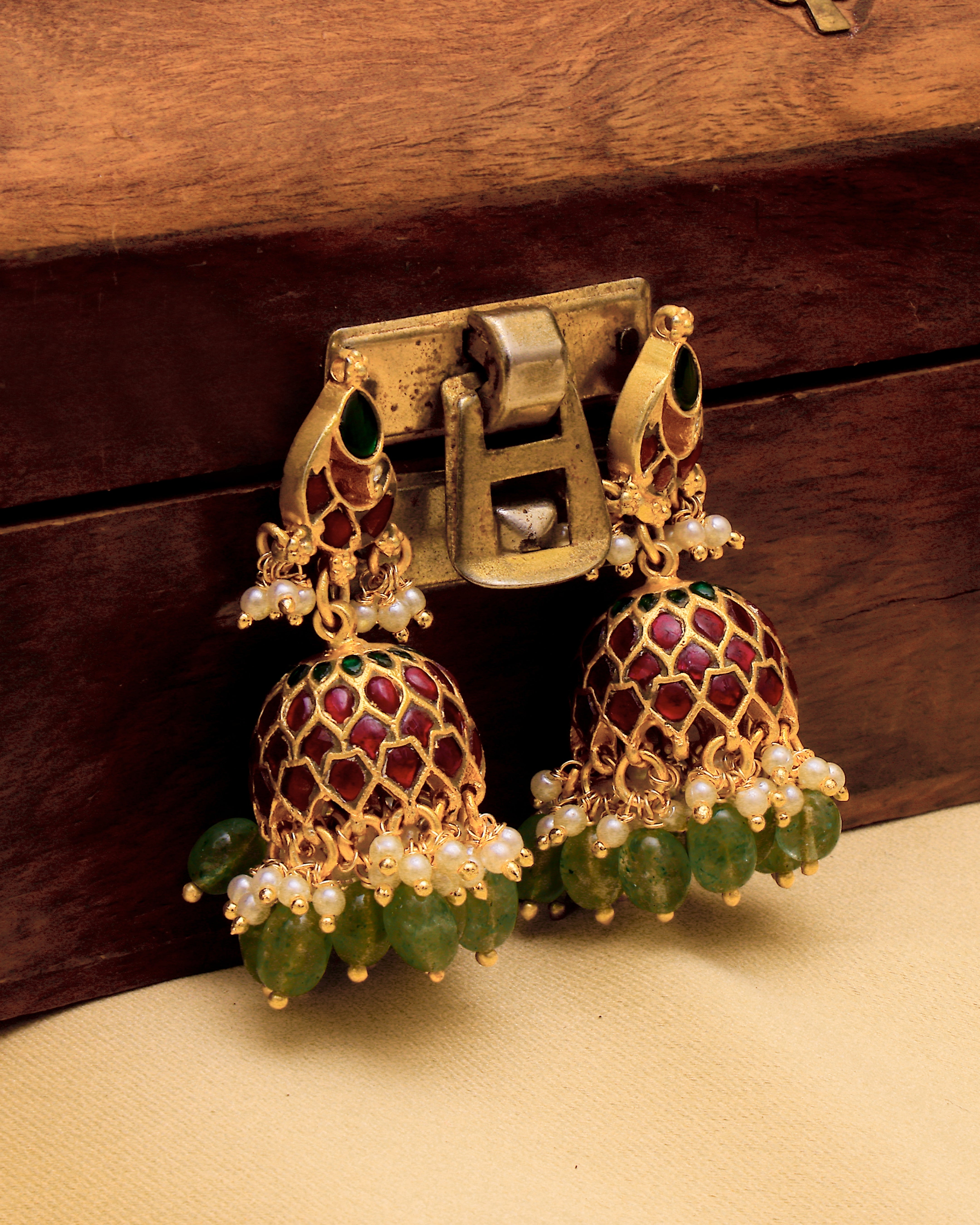 Gold earrings with green and red stones on a wooden surface