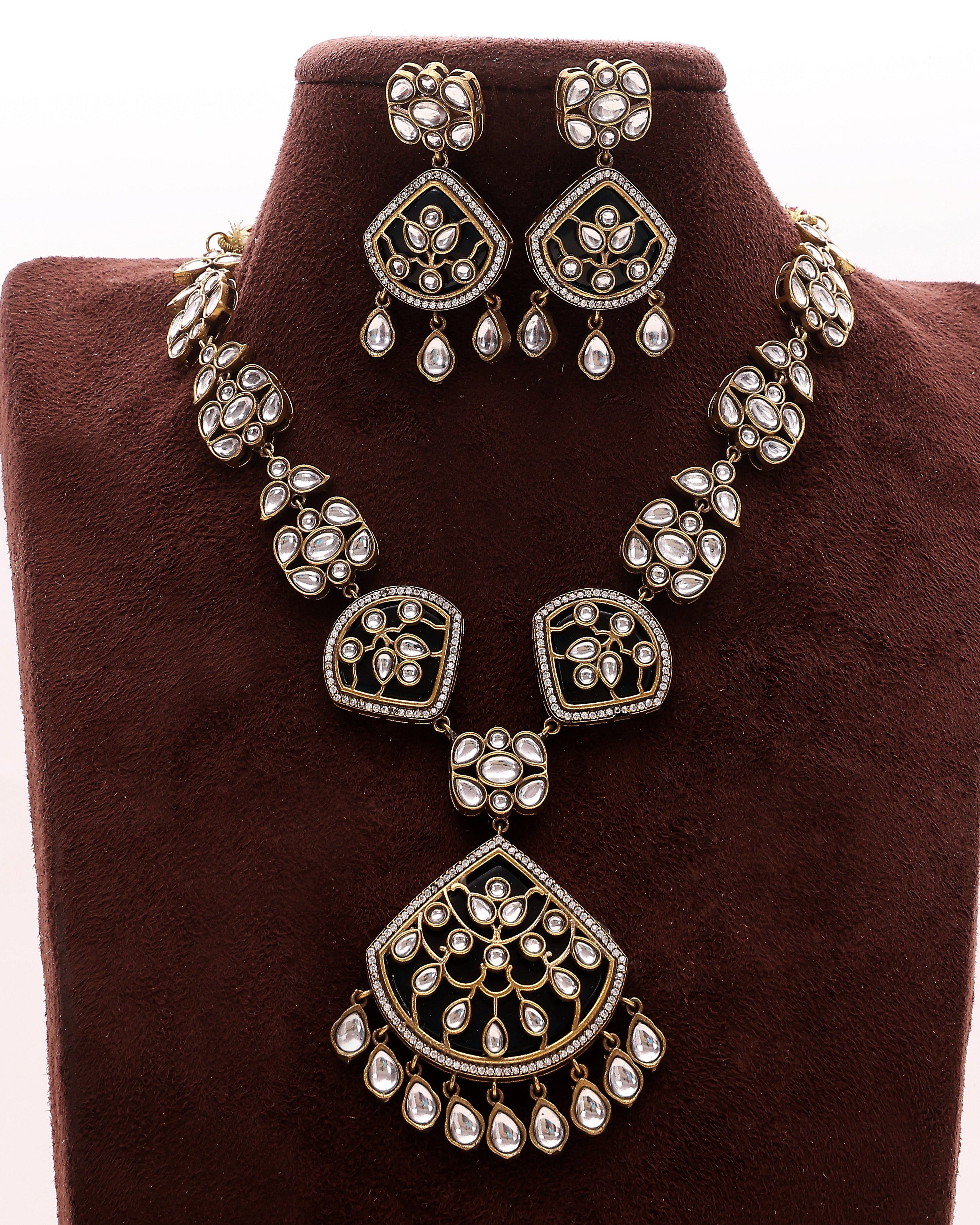 Ornate necklace and earrings set on a brown velvet stand
