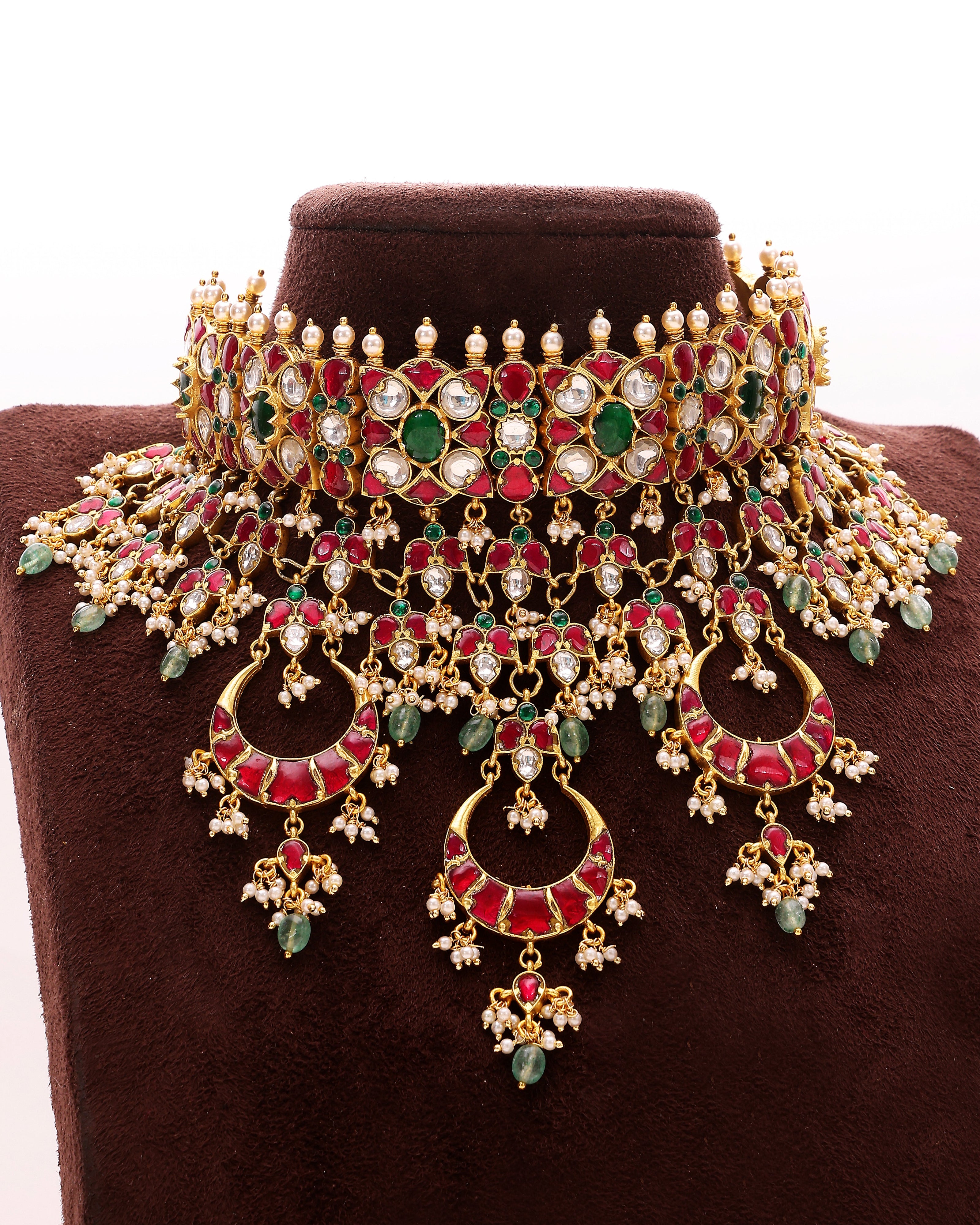 Ornate necklace with red, green, and gold colors on a brown stand.