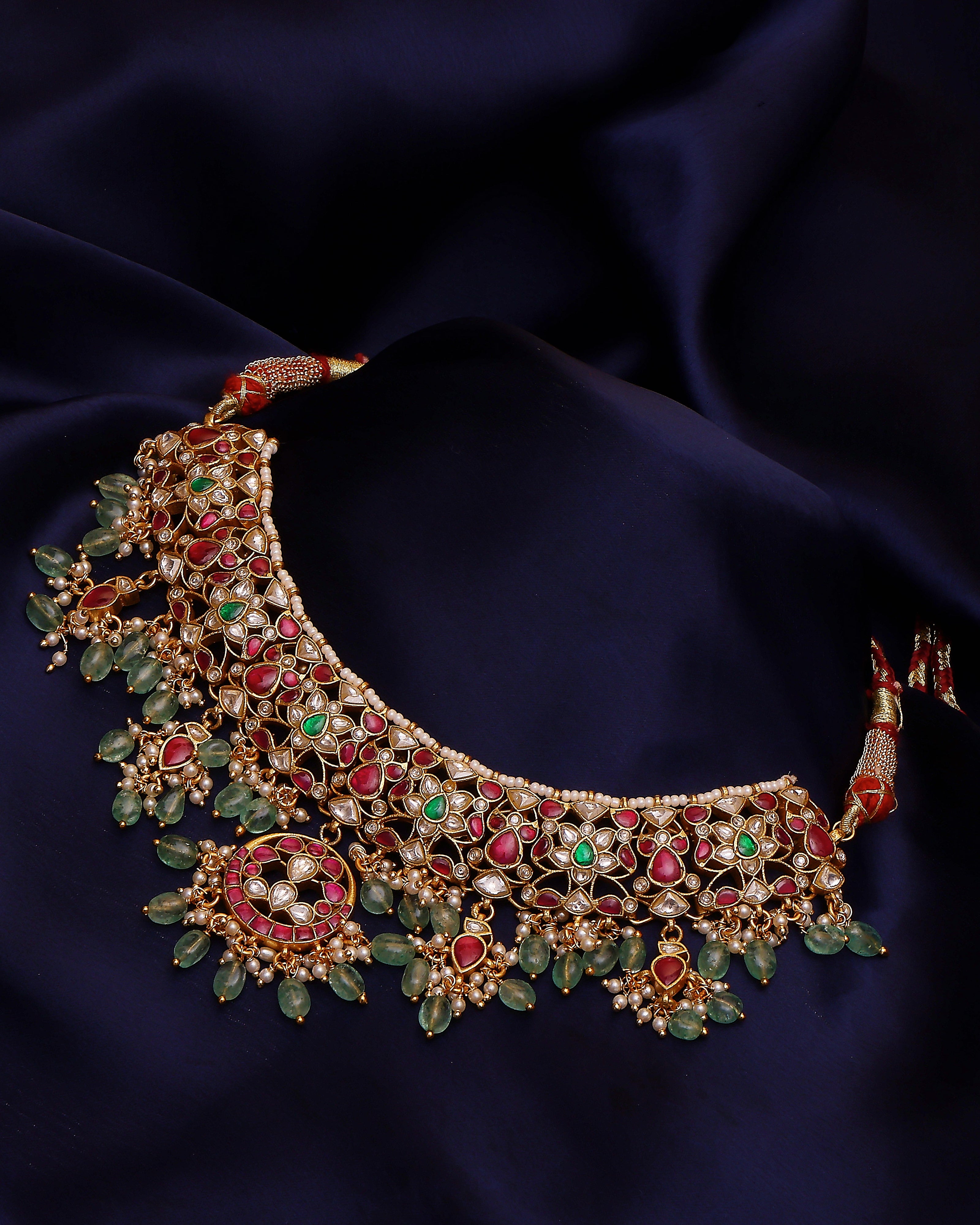 Ornate necklace with green, red, and gold stones on a dark blue fabric background