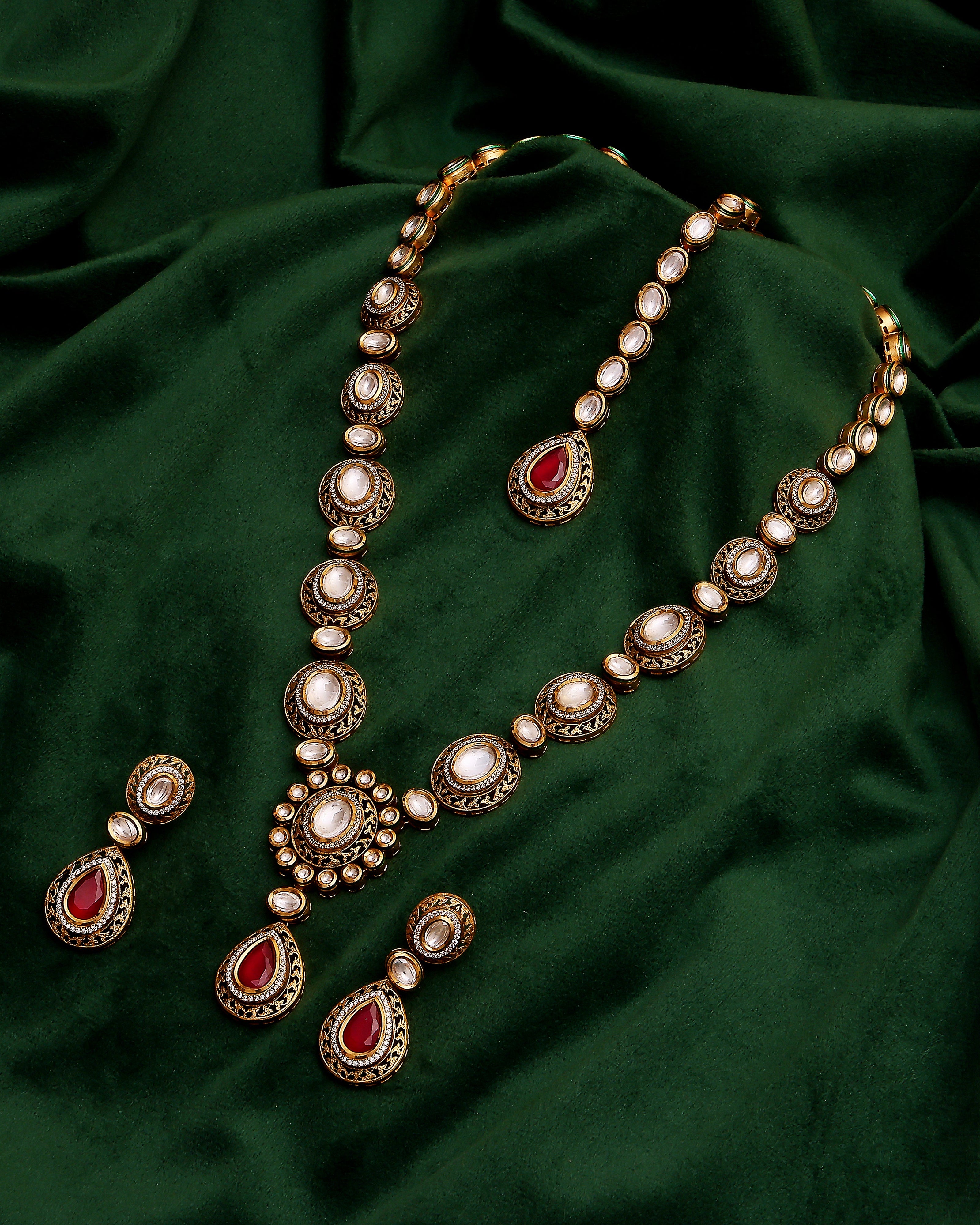 Ornate necklace and earrings set on a dark green fabric background