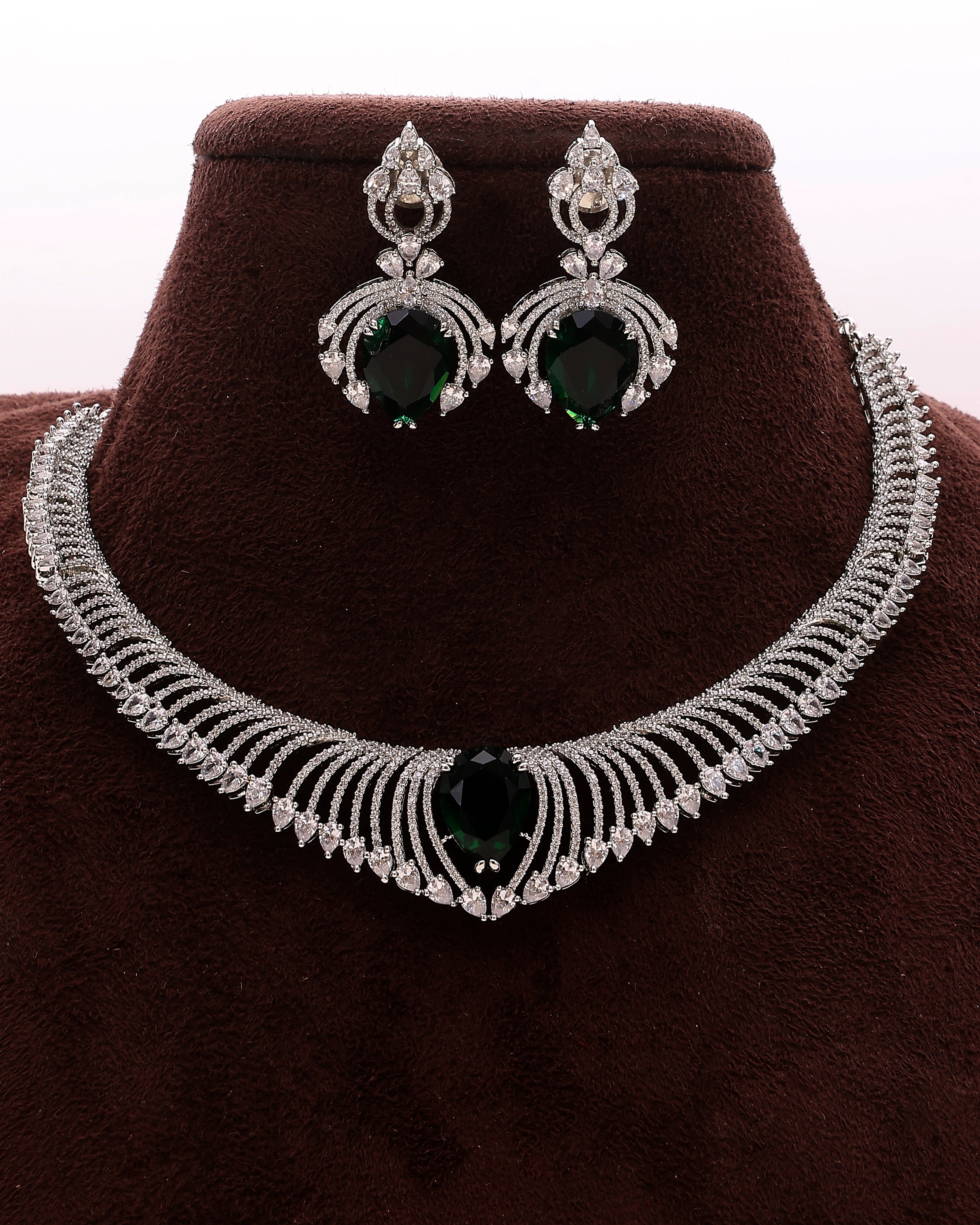 Jewelry set with necklace and earrings featuring green gemstones on a brown velvet stand.