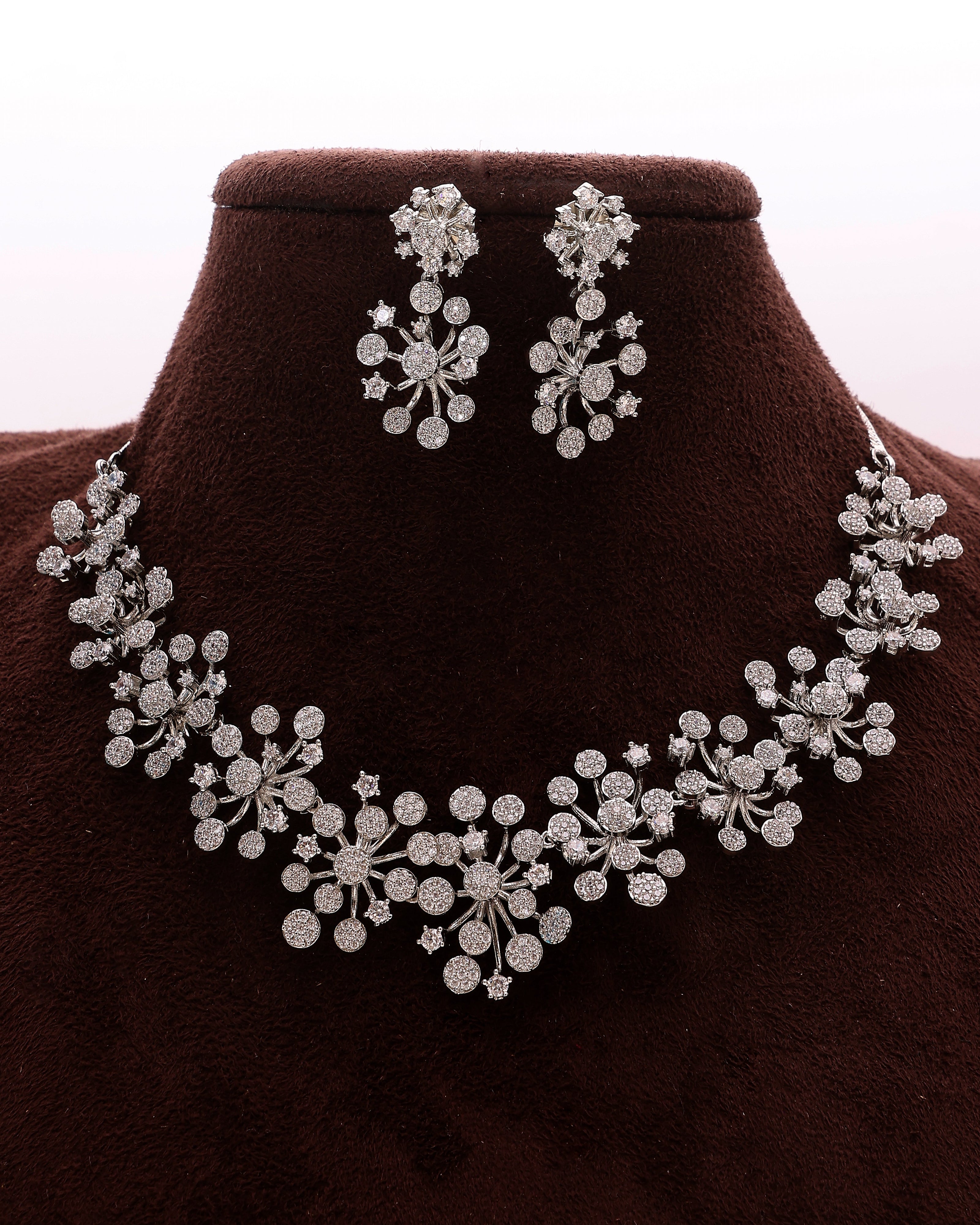 Silver necklace and earrings set on a brown velvet stand