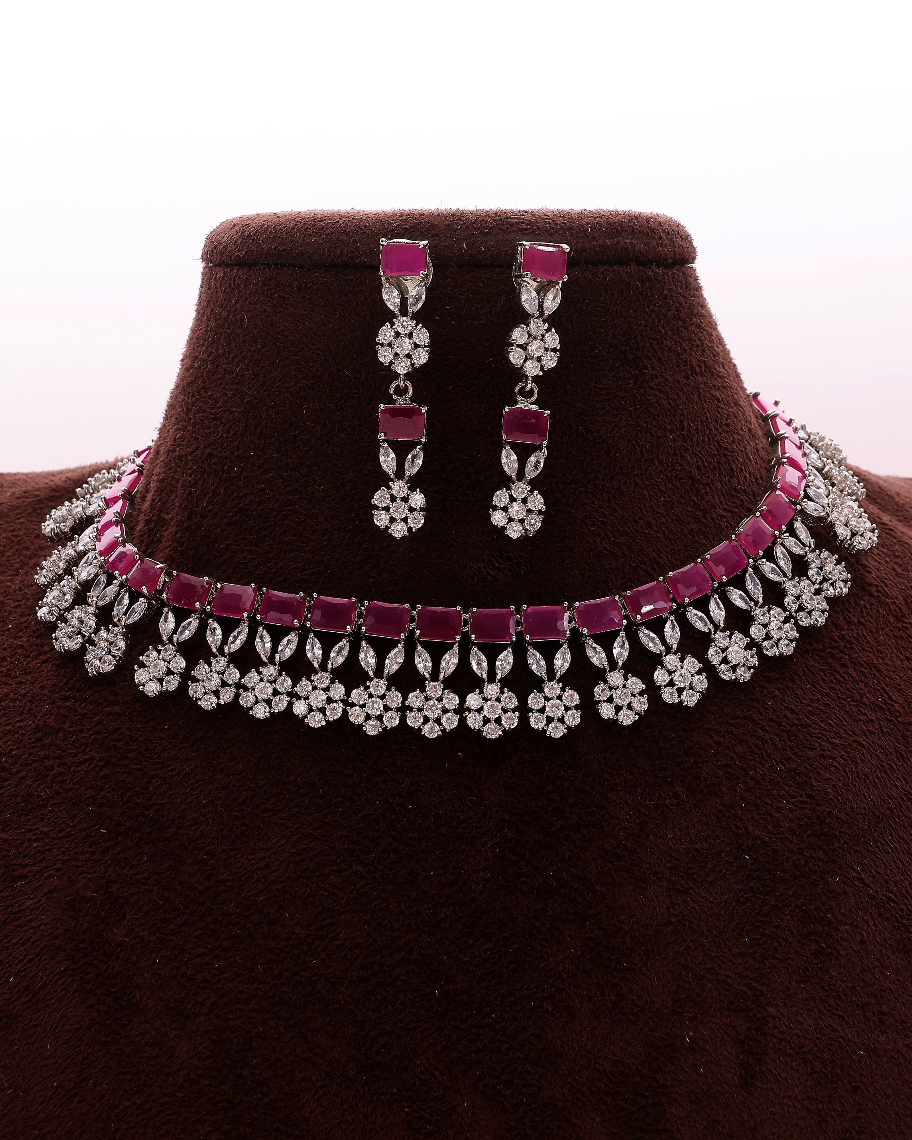 Jewelry set with pink and silver necklace and earrings on a brown stand.