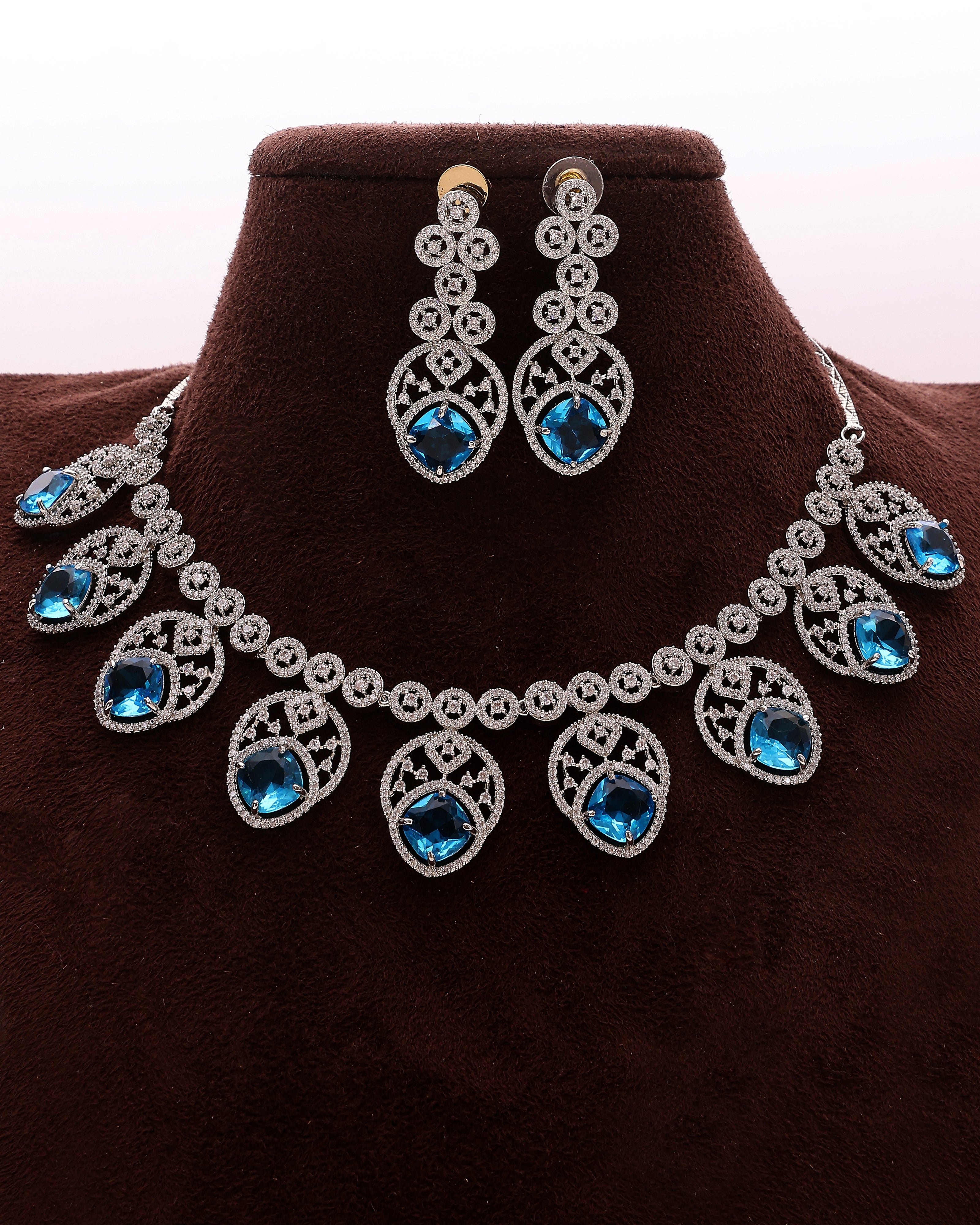 Jewelry set with necklace and earrings featuring blue gemstones on a brown stand.