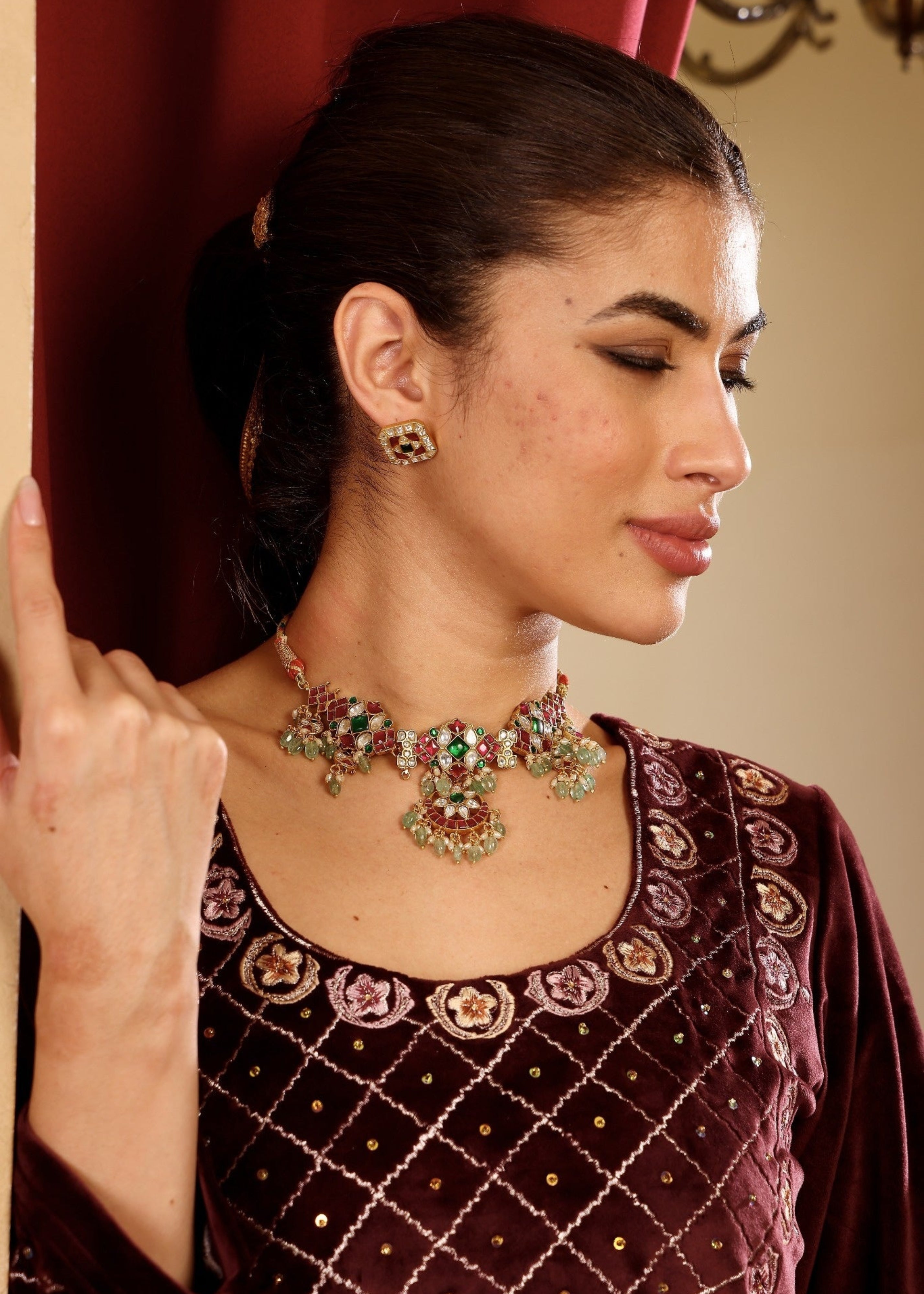 Woman wearing a detailed necklace and traditional outfit with a red curtain background
