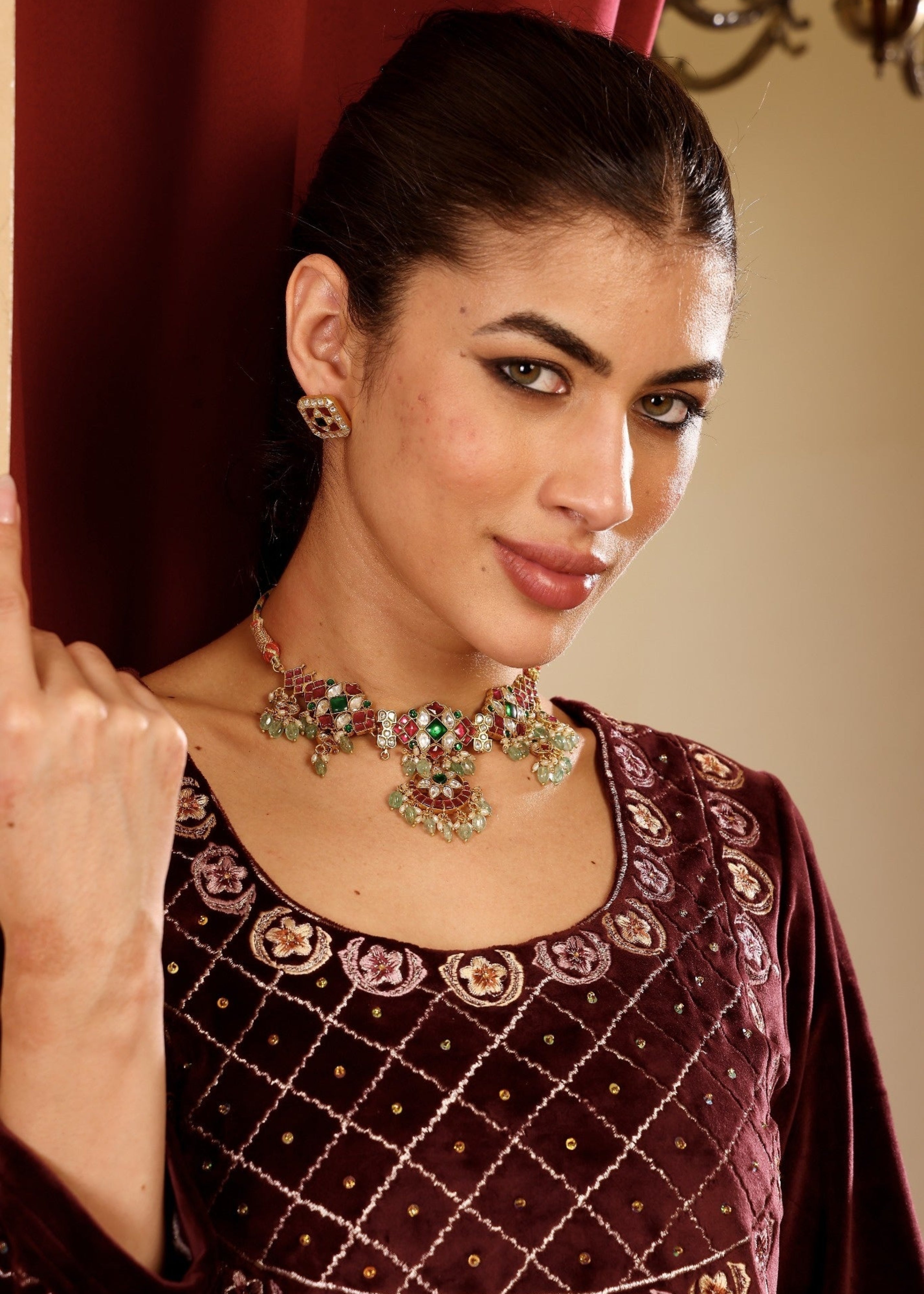 Woman wearing a dark red embroidered outfit with a colorful necklace indoors.