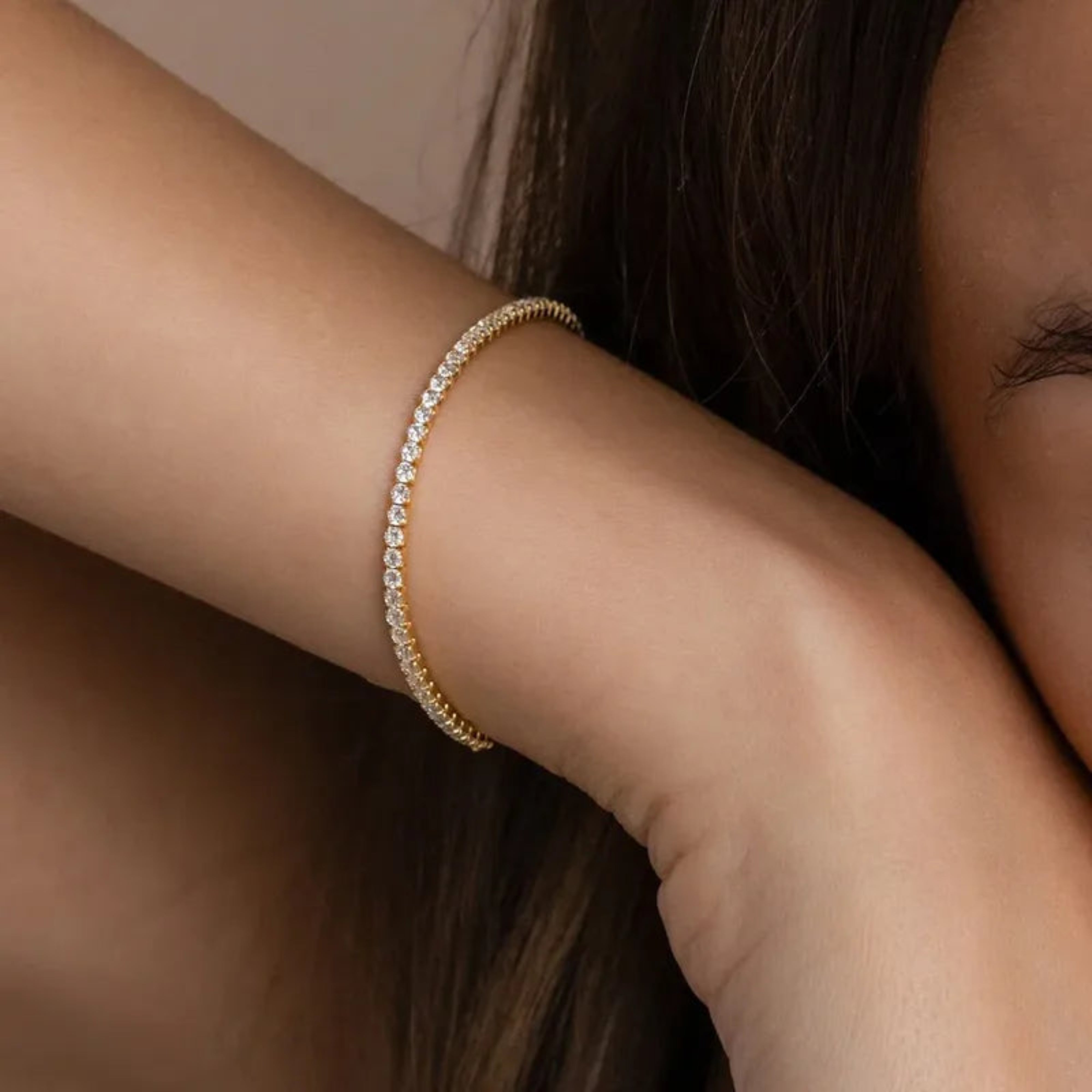 Gold bracelet with clear stones on a wrist against a neutral background