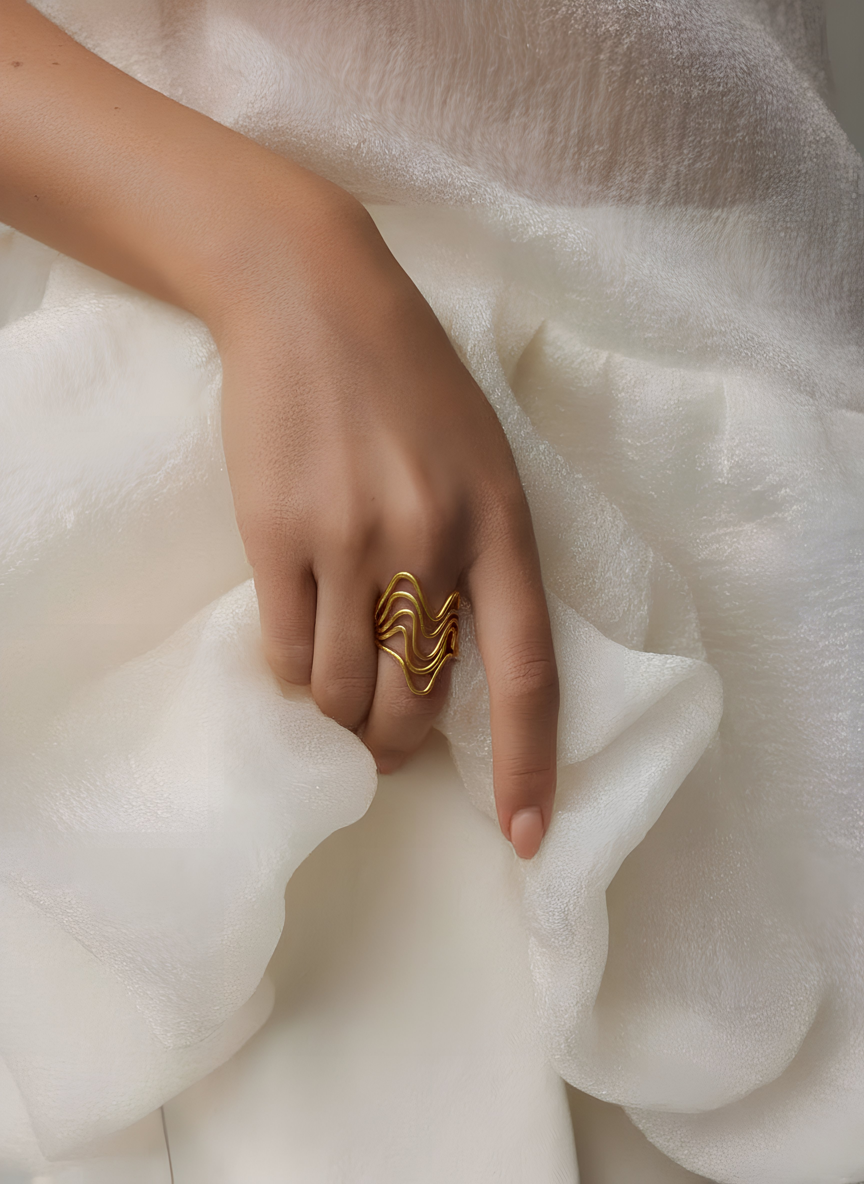 Hand wearing a gold ring on white fabric