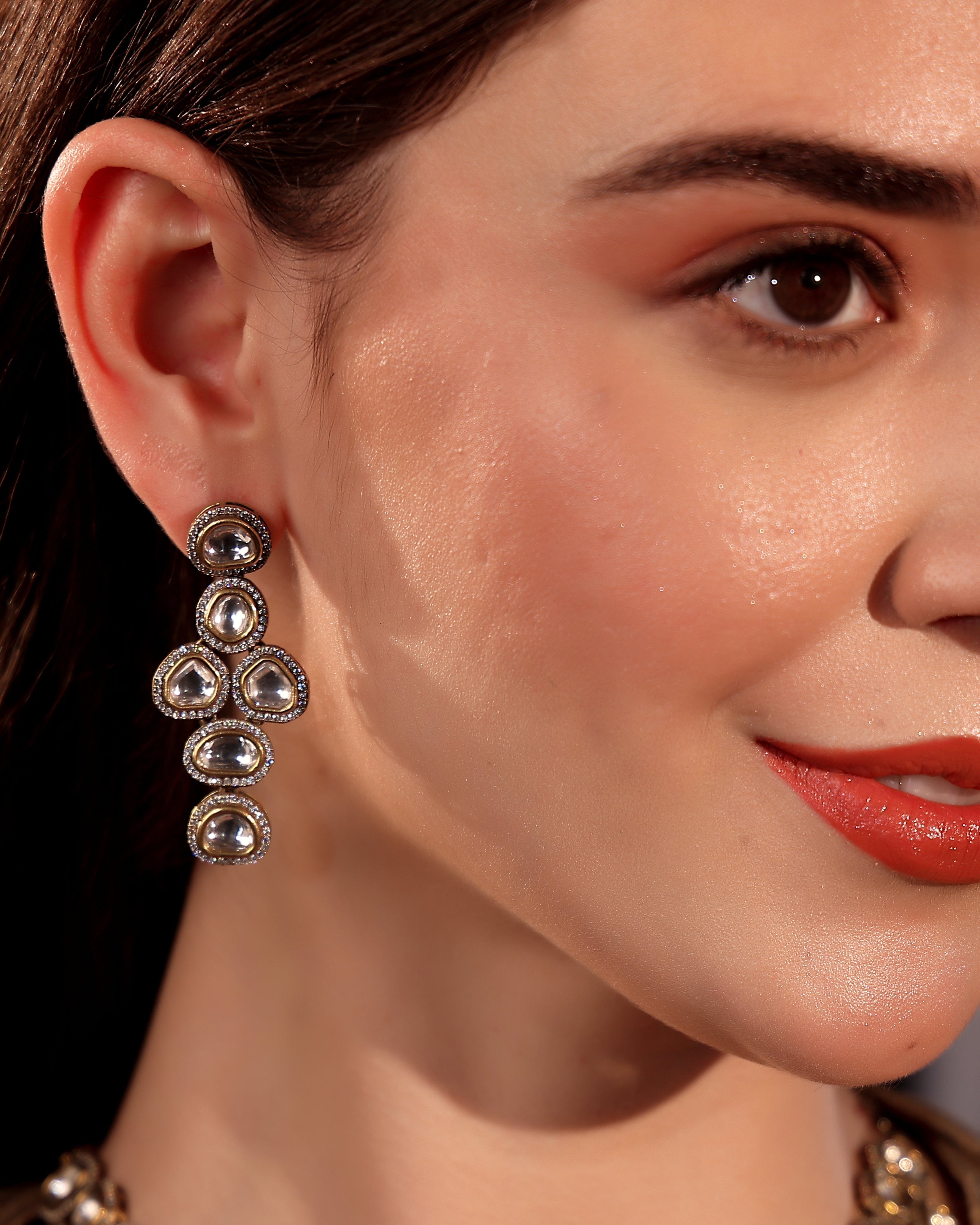 Close-up of a woman wearing a pair of dangling earrings with a neutral background