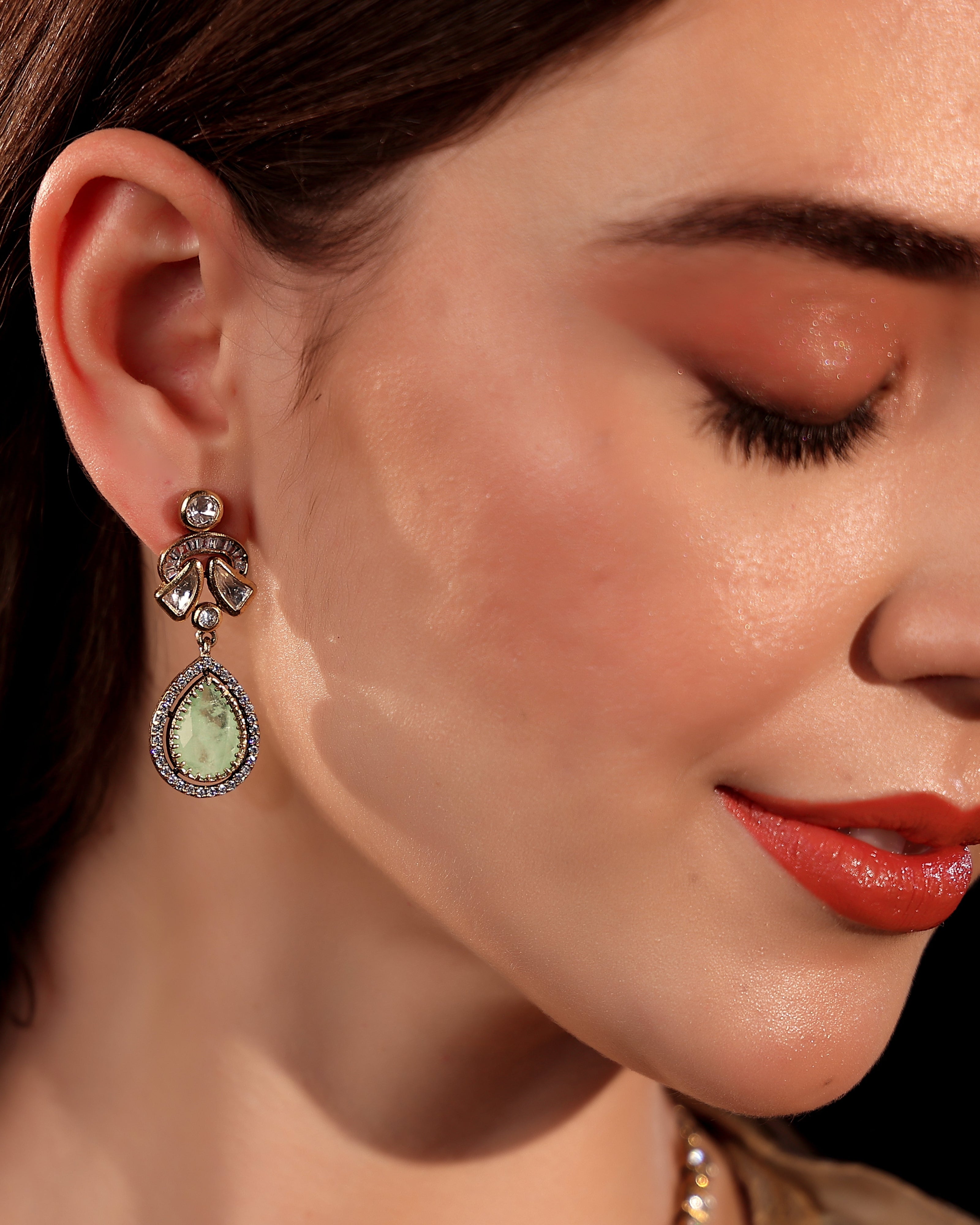 Close-up of a woman wearing a teardrop-shaped earring with a green gemstone.