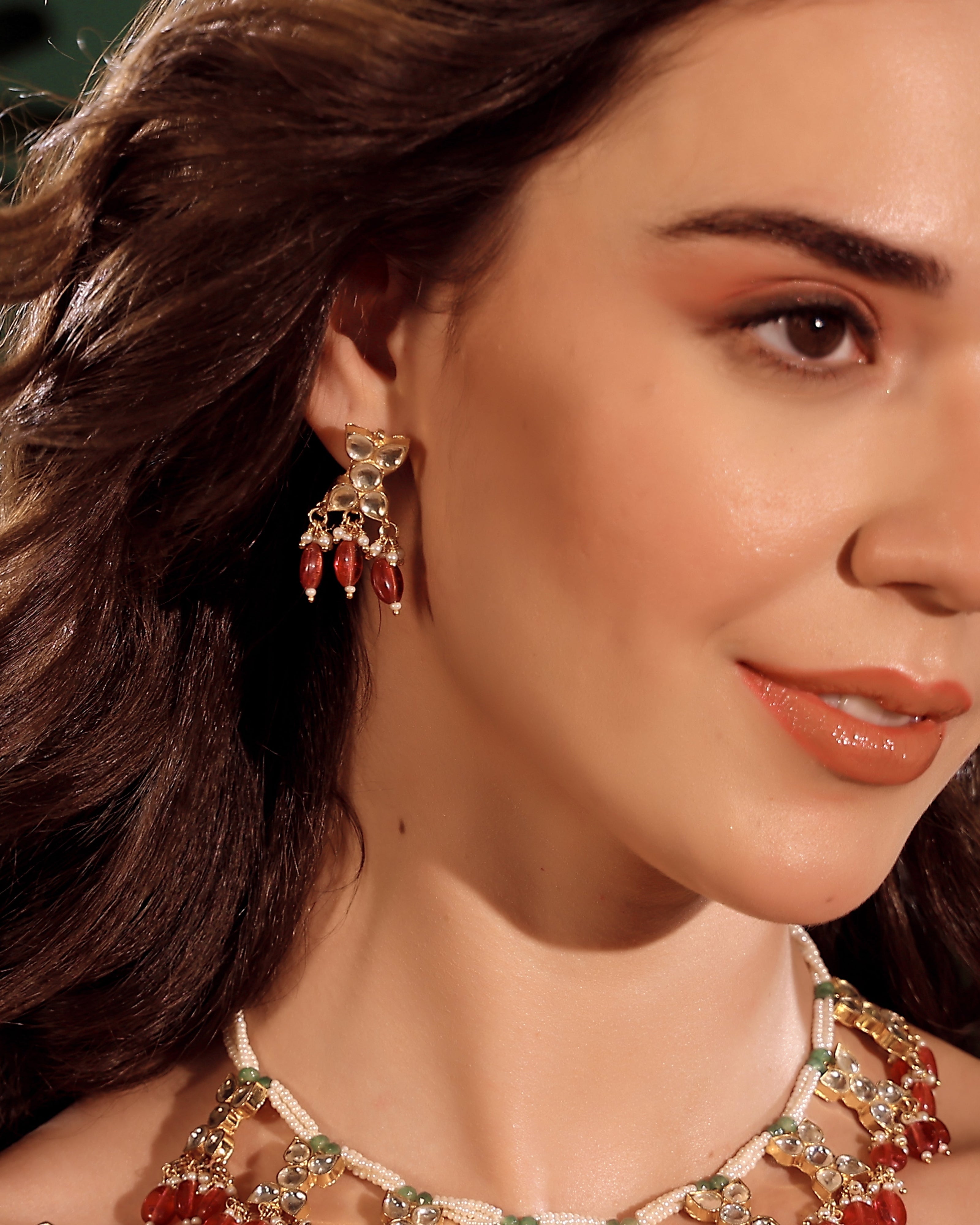 Close-up of a woman wearing gold earrings with red stones and a matching necklace.