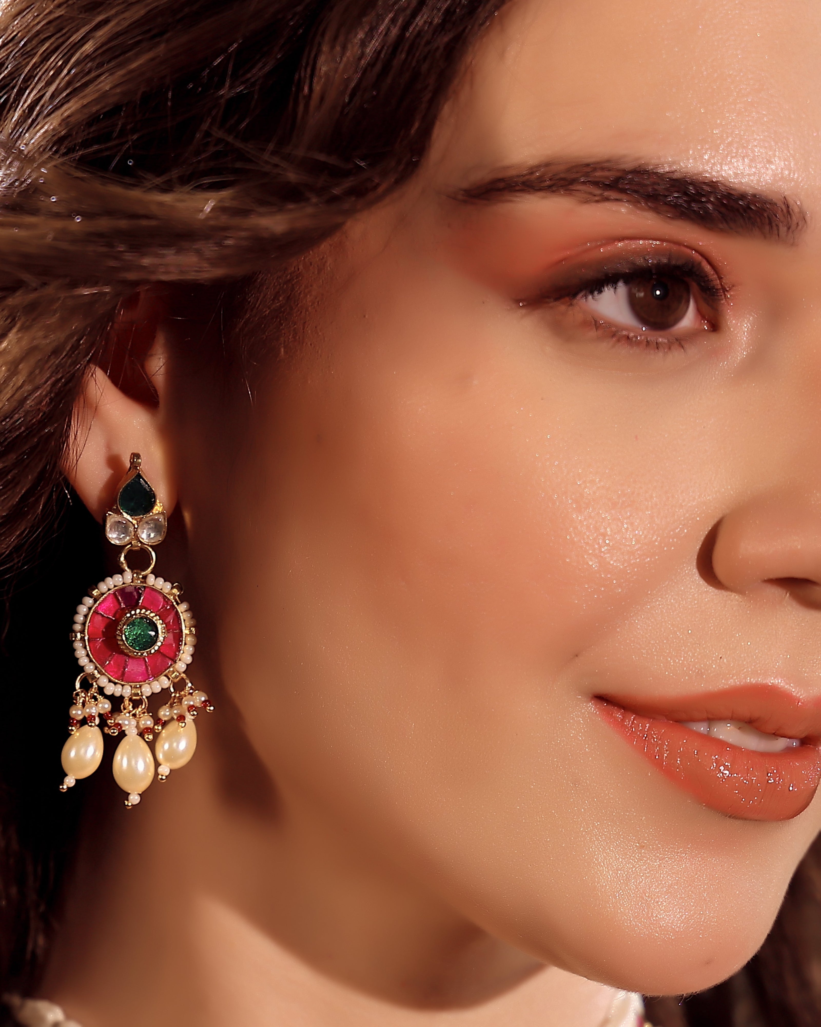 Close-up of a woman wearing an ornate earring with red, green, and gold colors.