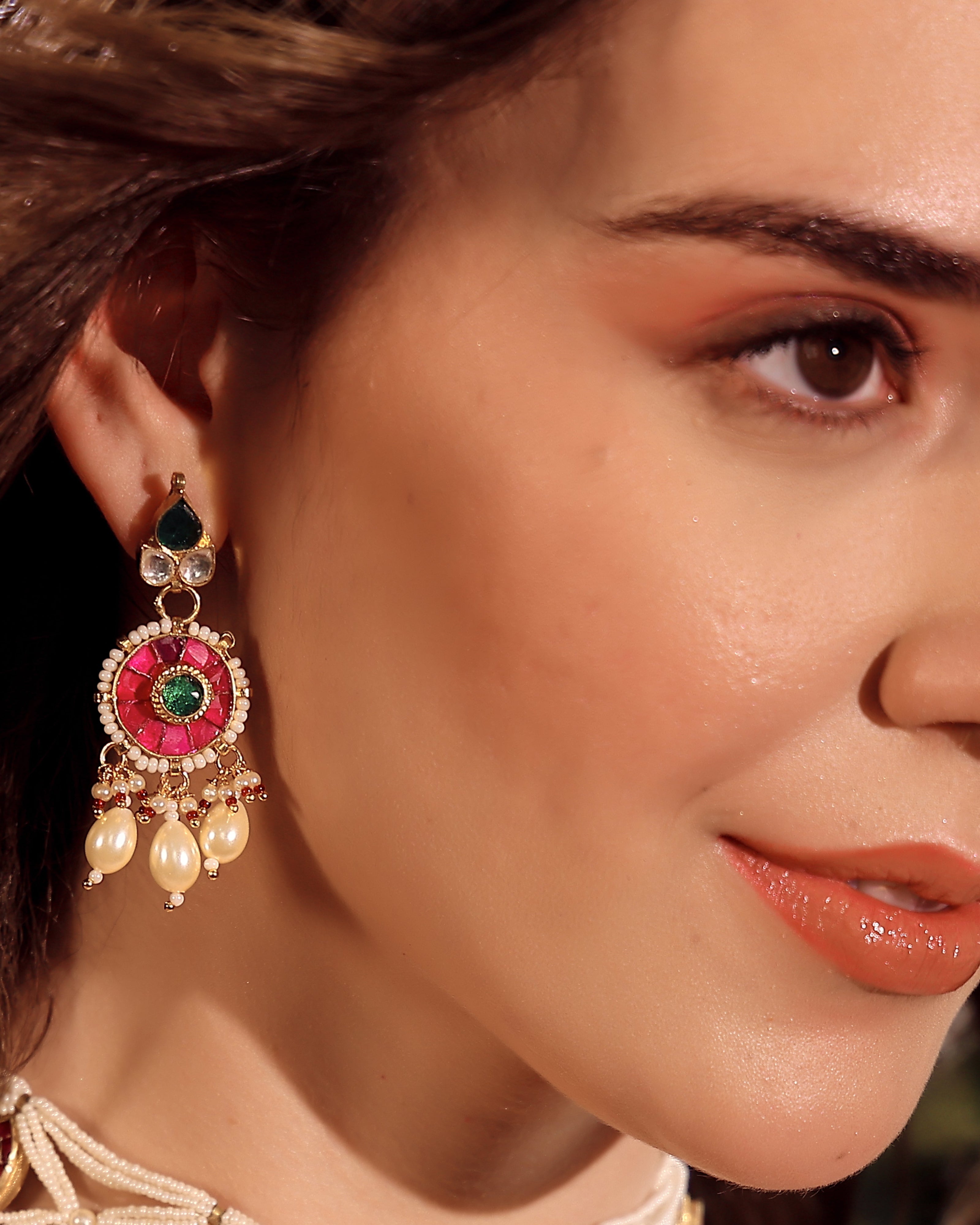 Close-up of a woman wearing an ornate earring with red, green, and gold colors.