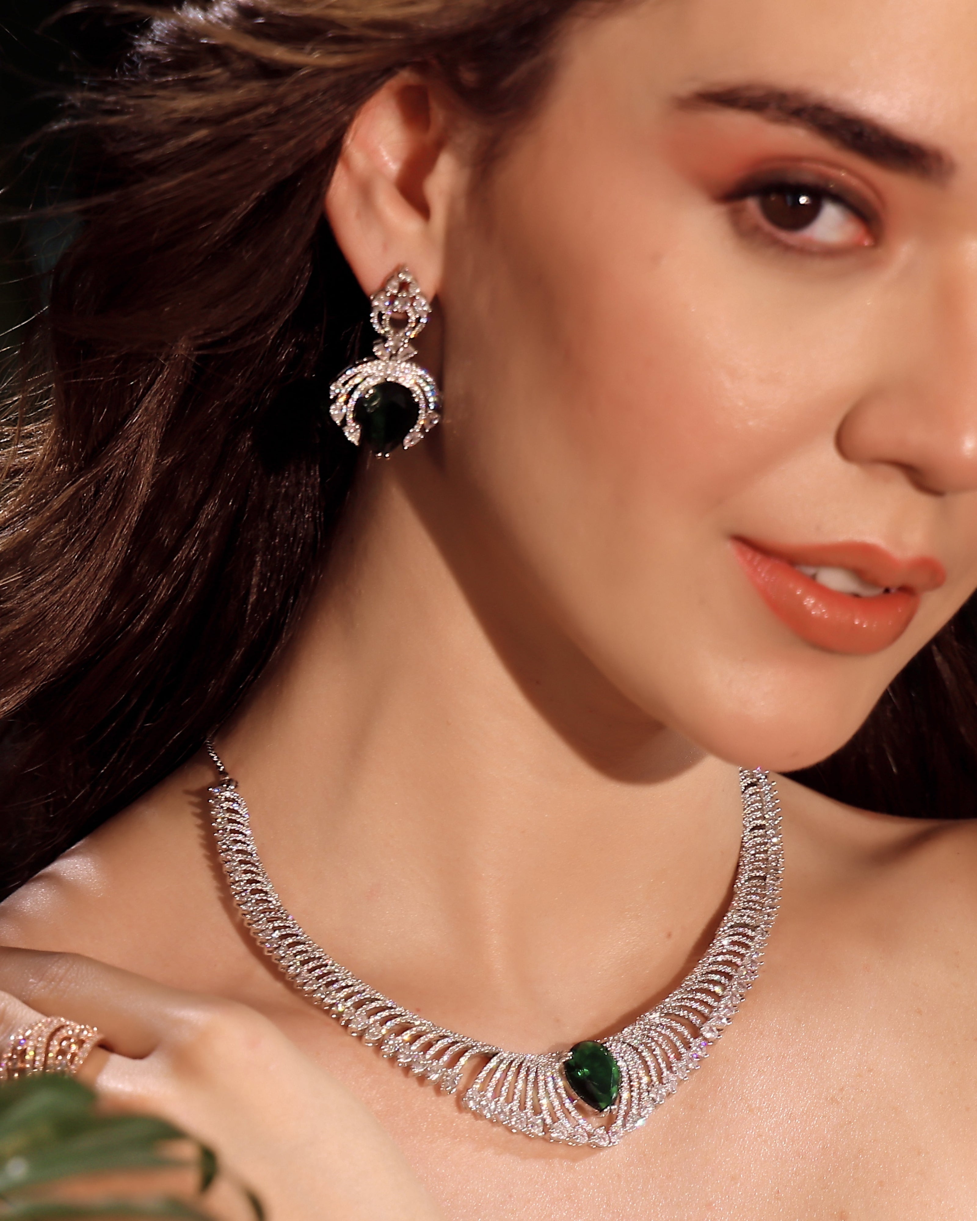 Close-up of a woman wearing a silver necklace with green gemstones and matching earrings.