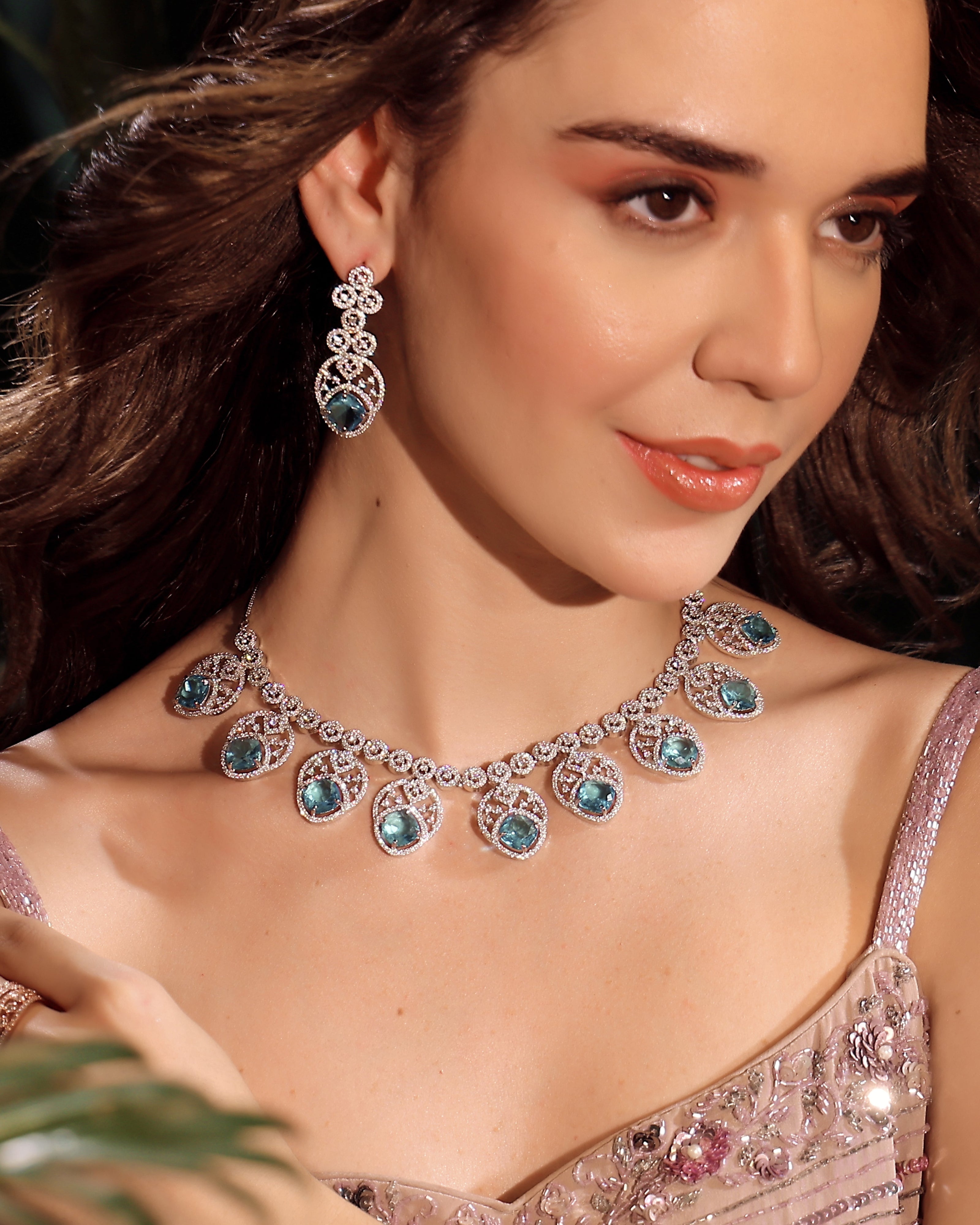 Woman wearing a luxurious diamond and gemstone necklace and earrings.