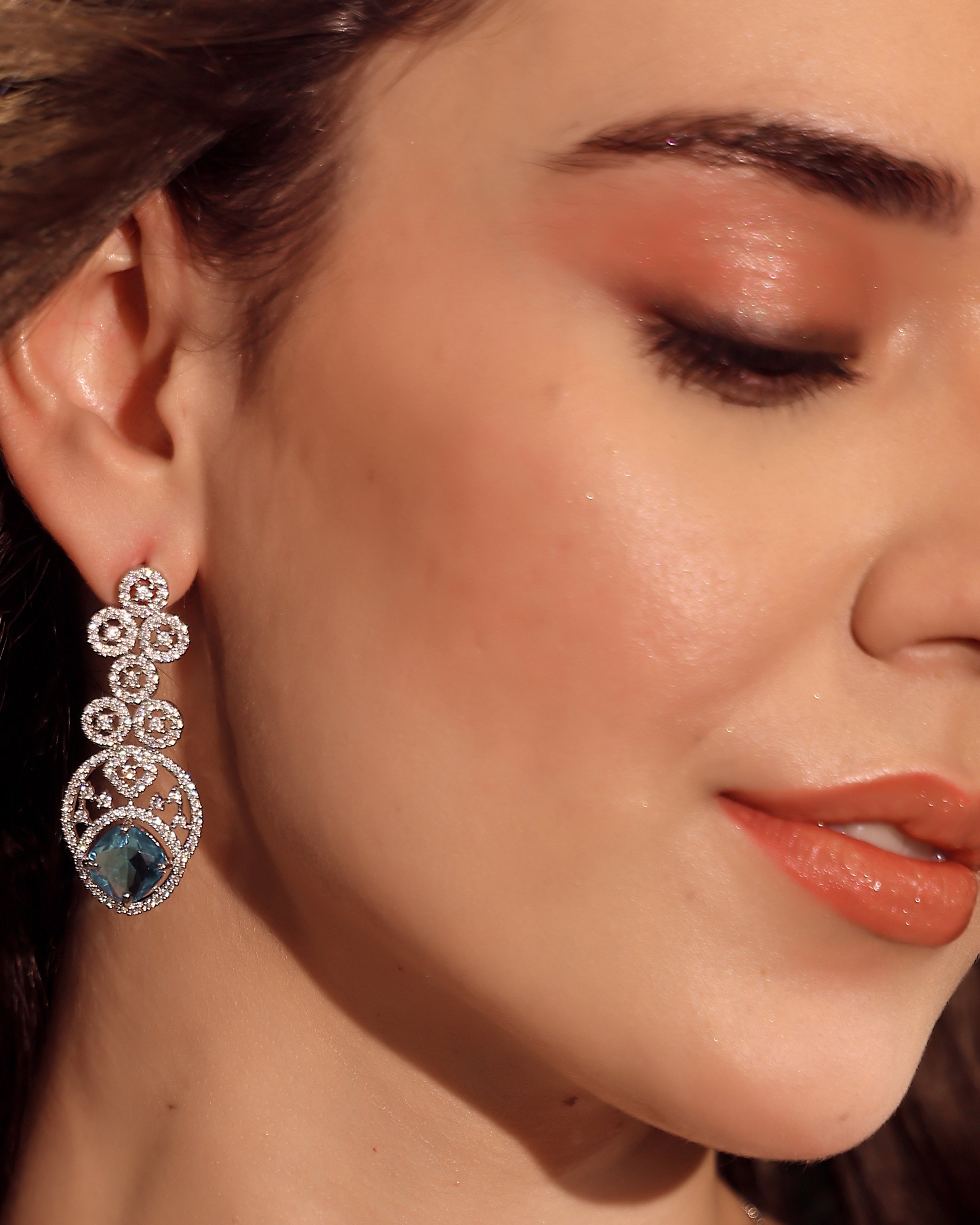 Close-up of a woman wearing a decorative earring with a blue gemstone.