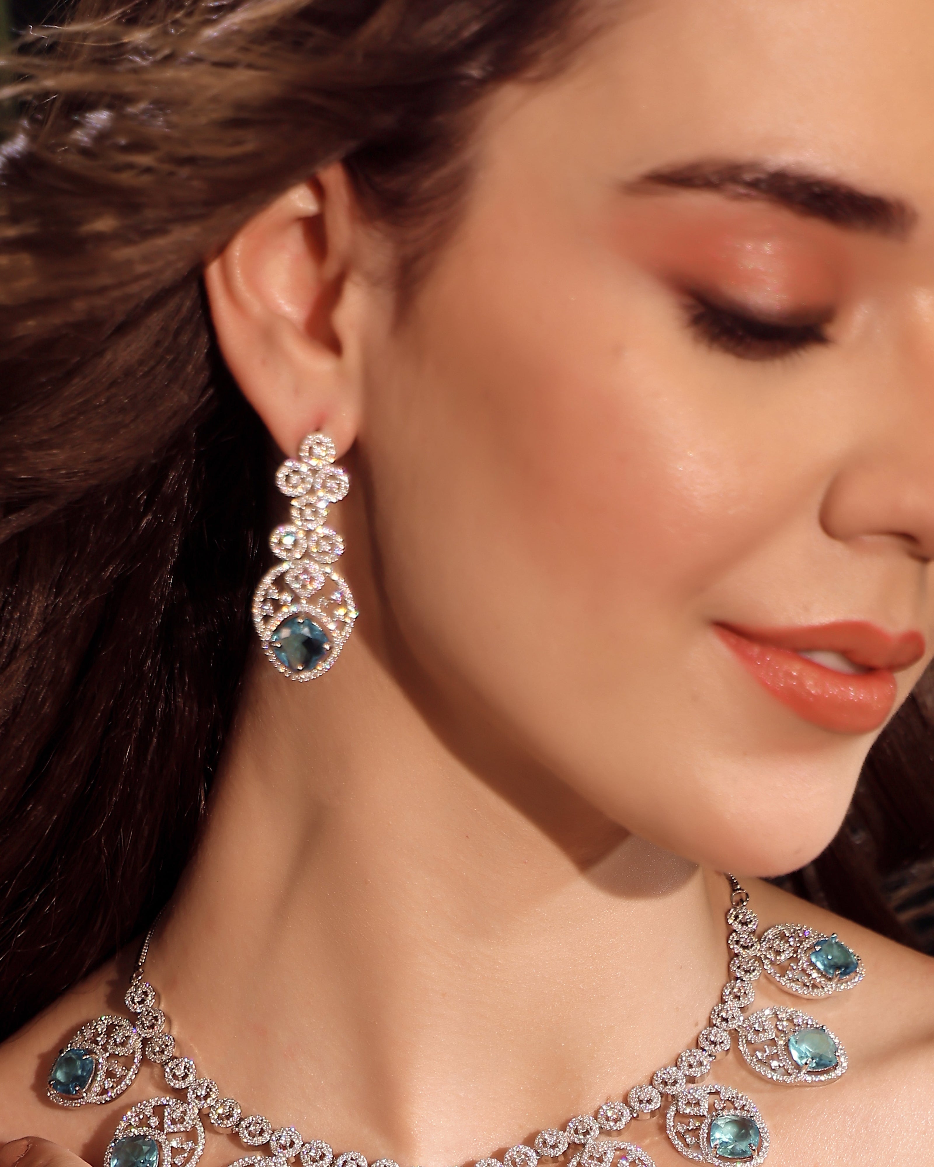 Close-up of a woman wearing a diamond and emerald necklace and earrings.