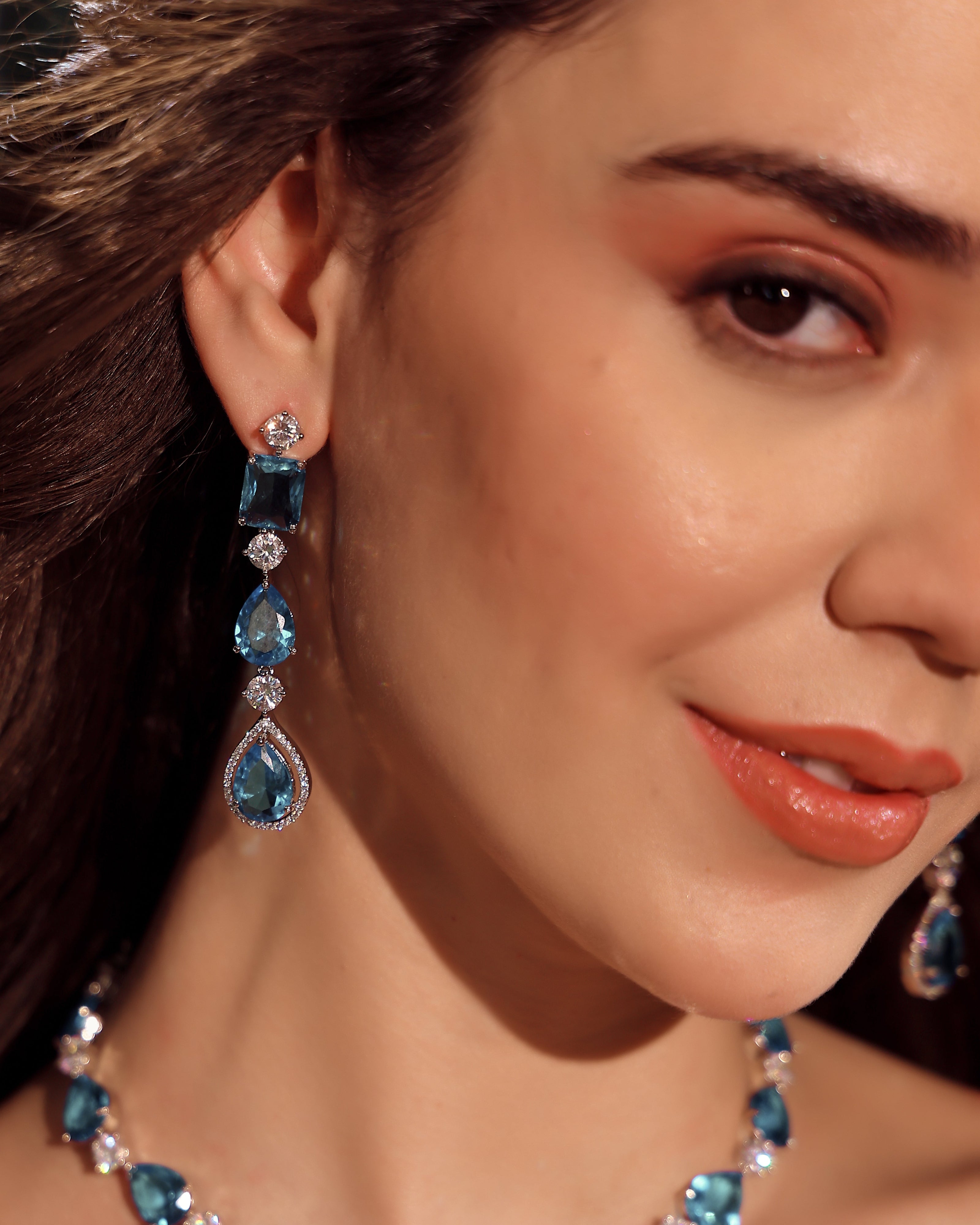 Close-up of a woman wearing blue gemstone earrings and necklace.