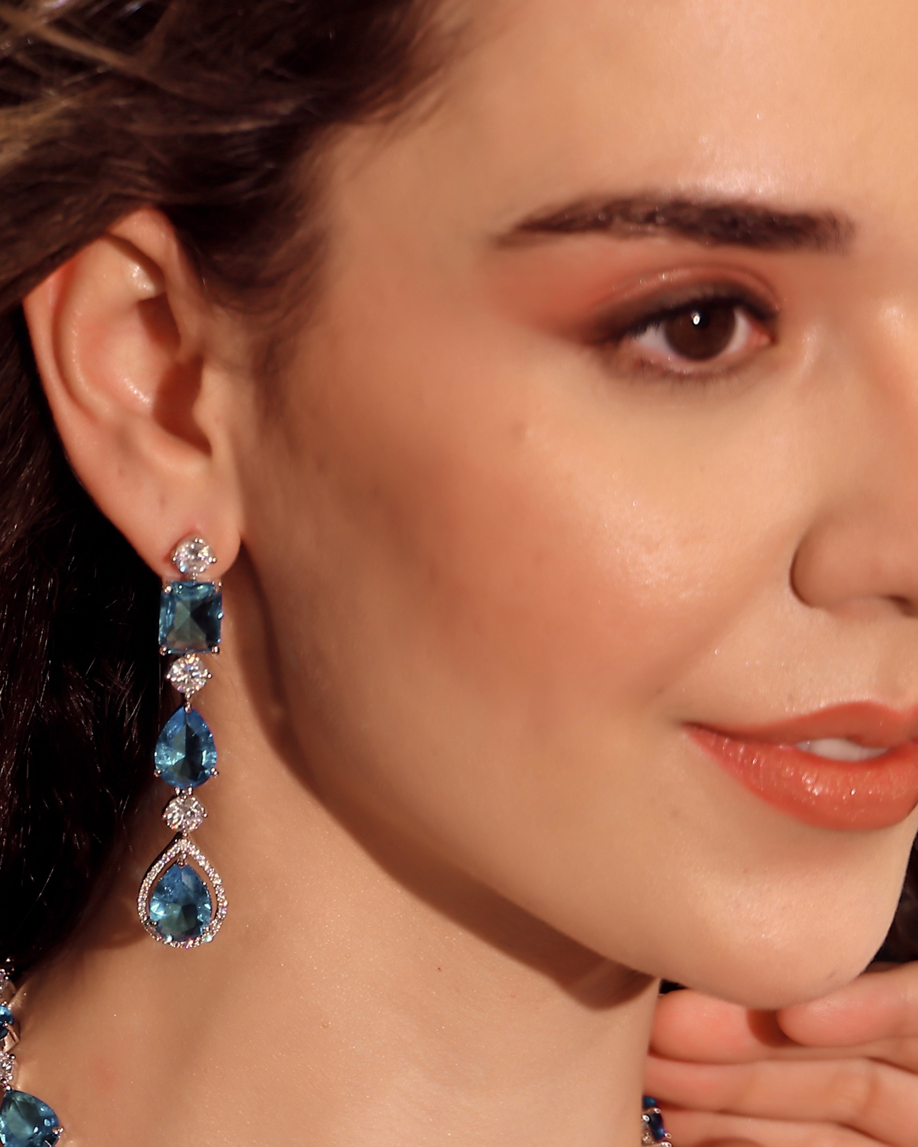 Close-up of a woman wearing blue gemstone earrings with a blurred background