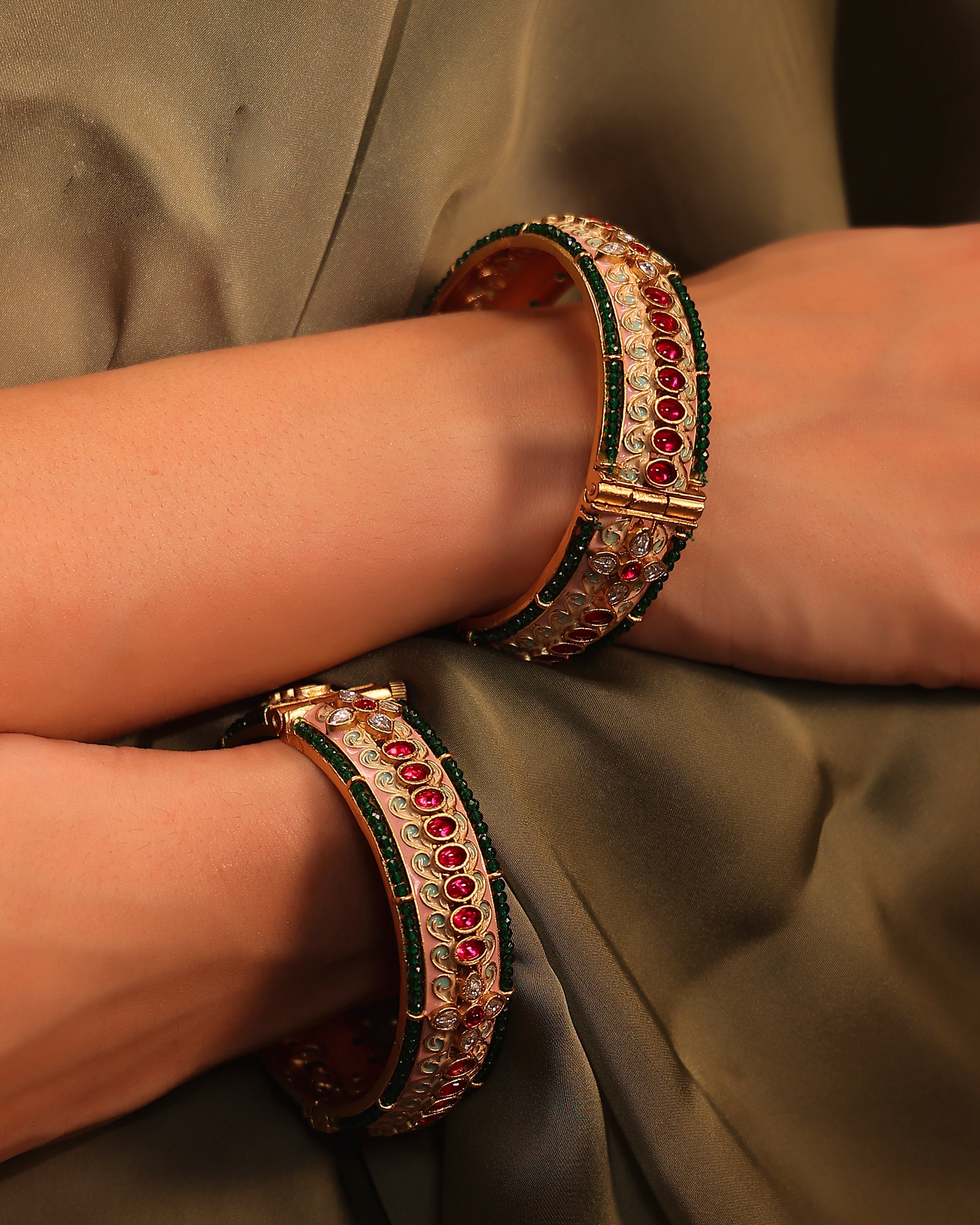 Close-up of a person wearing two ornate bangles with gemstones on a plain background