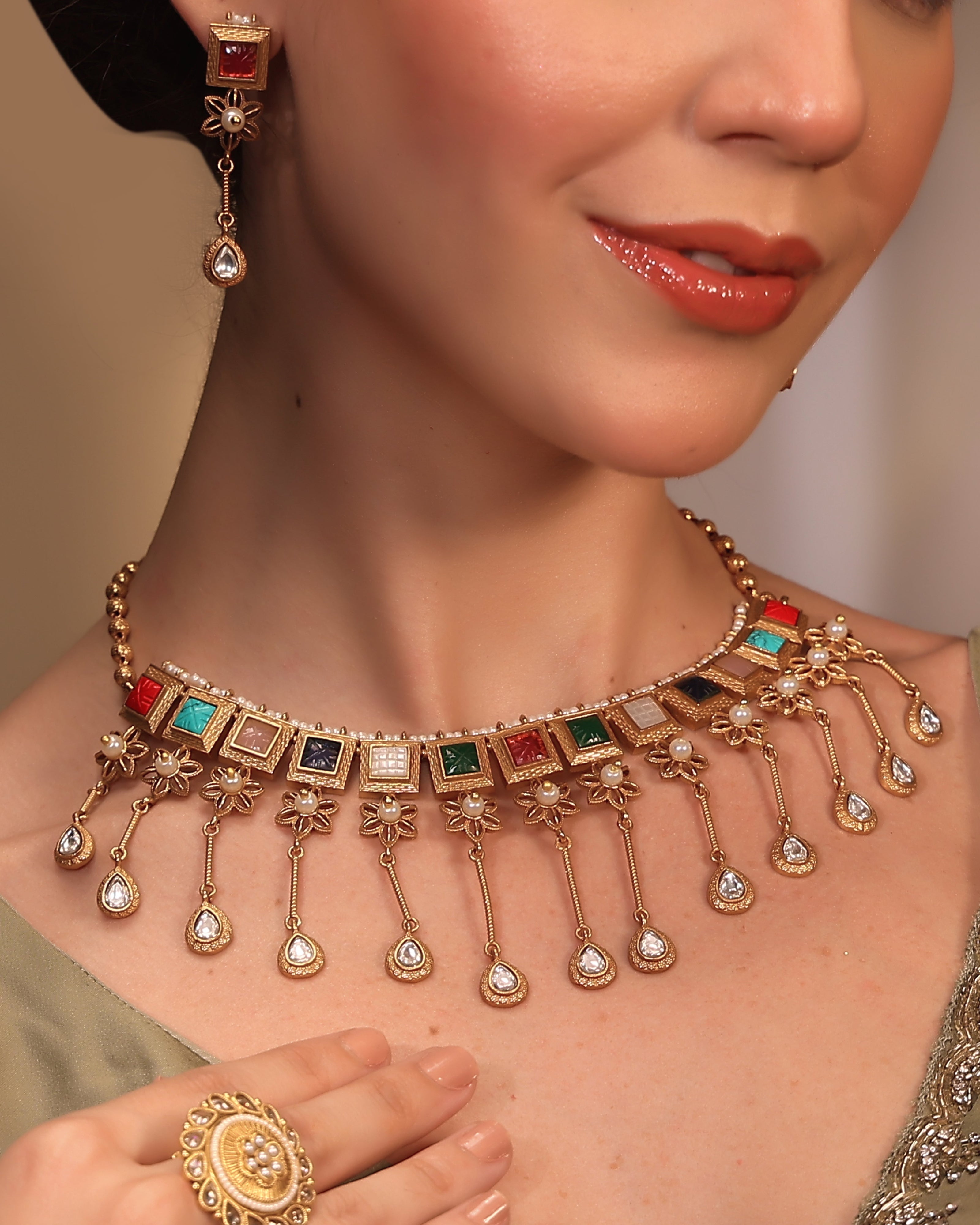 Close-up of a woman wearing a gold necklace with colorful stones, earrings, and ring.