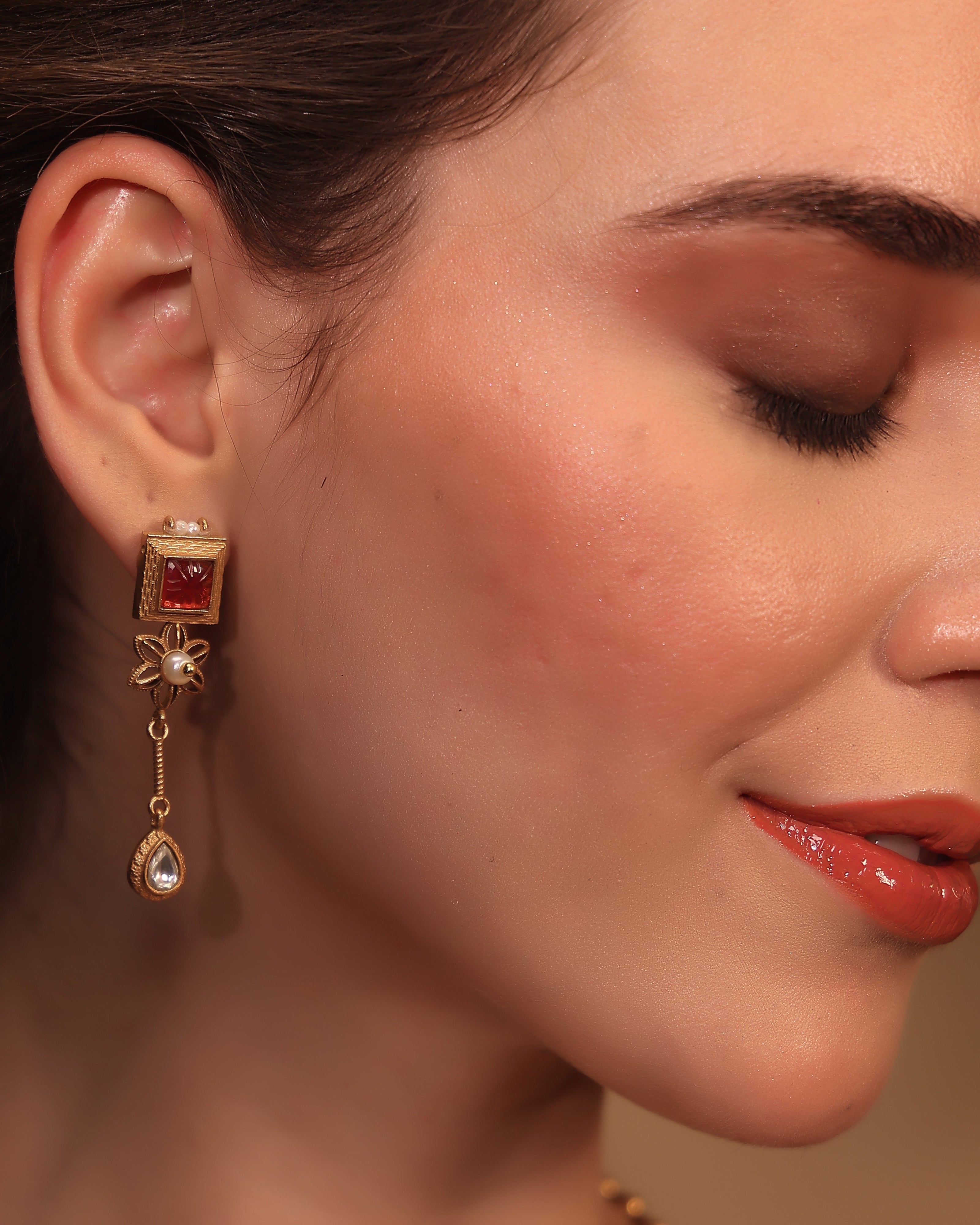 Close-up of a woman wearing a gold earring with a red gemstone.