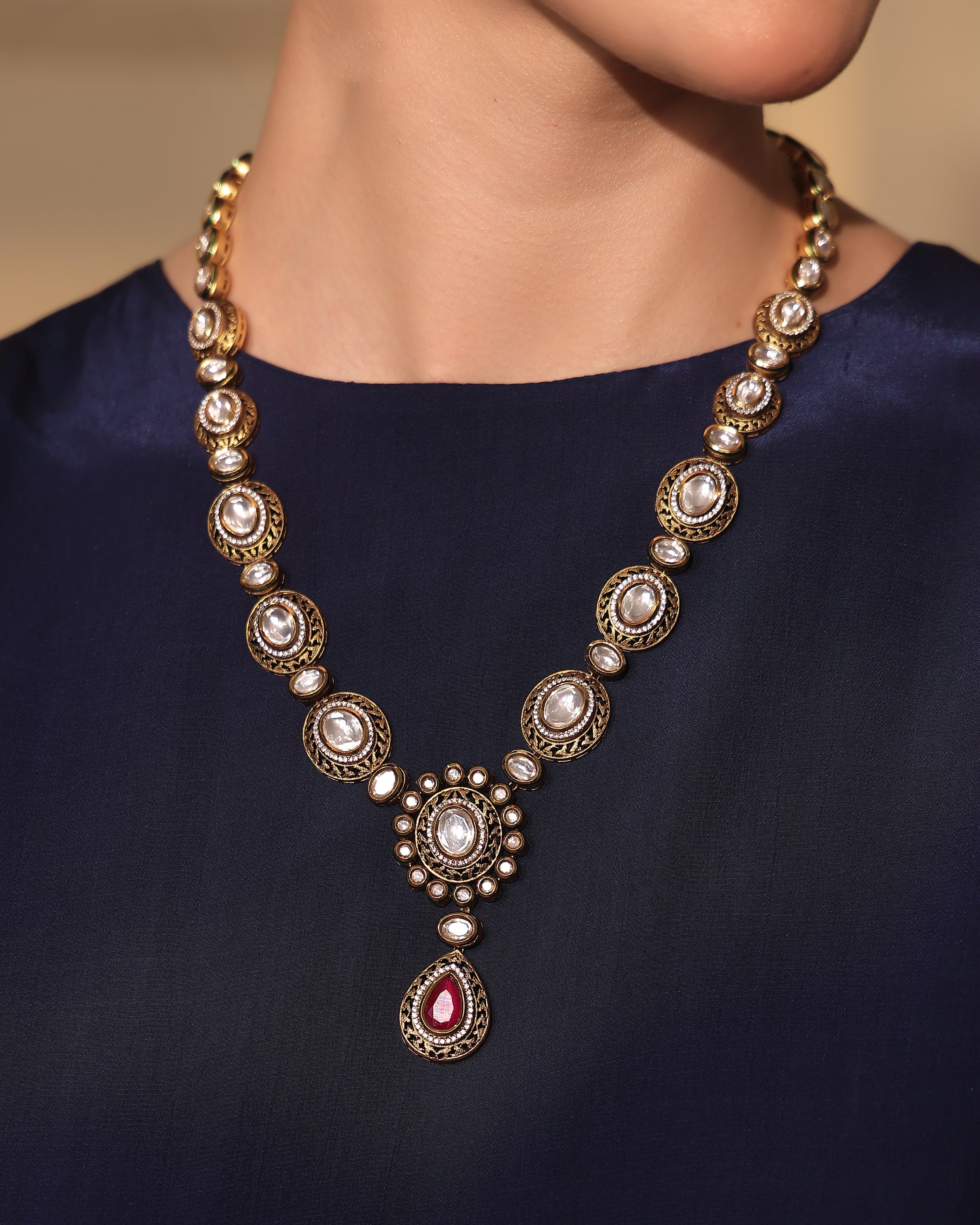 Elegant gold and pearl necklace with a red gemstone pendant on a person wearing a dark blue top.