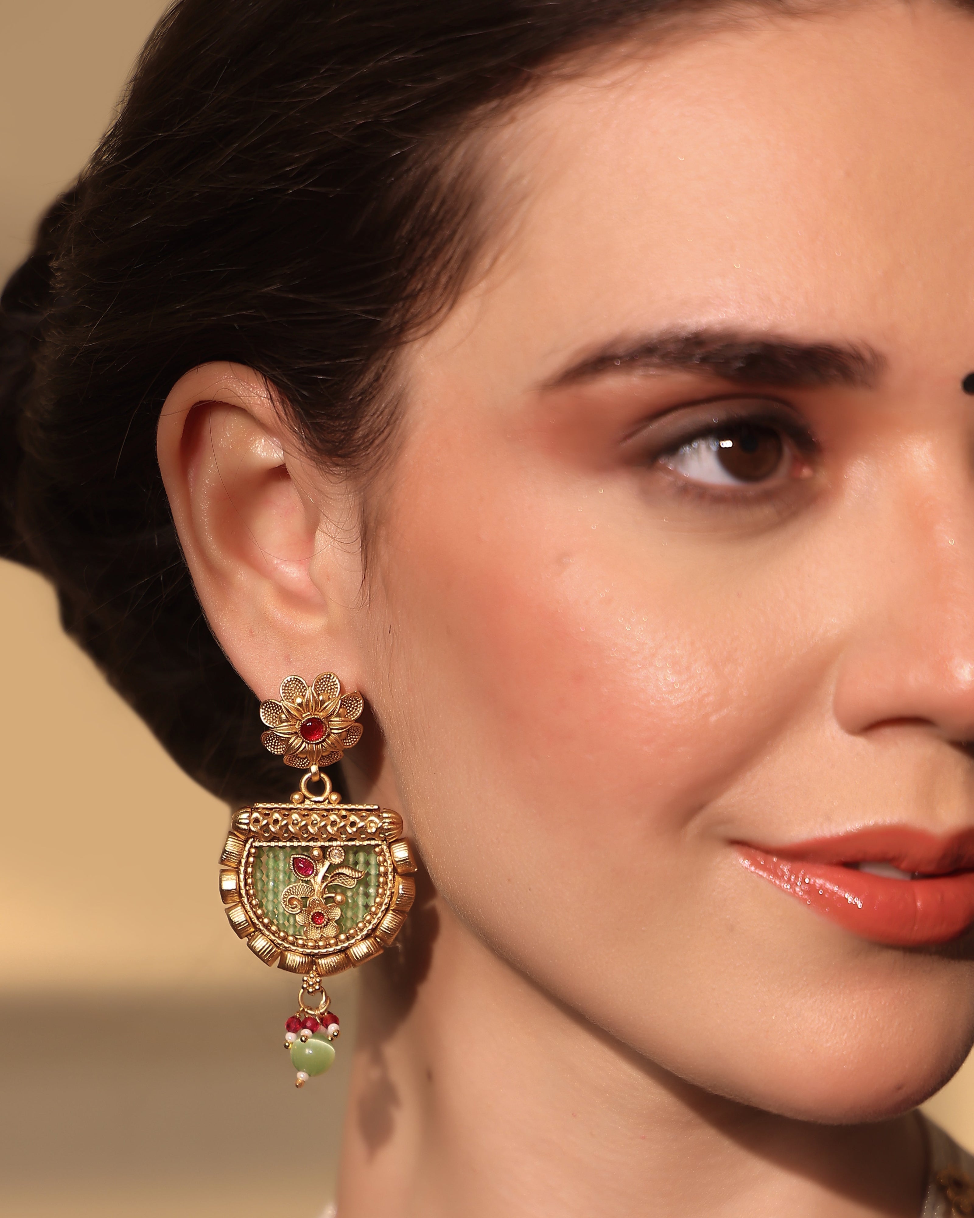 Close-up of a woman wearing an ornate earring with intricate design and colorful gemstones.