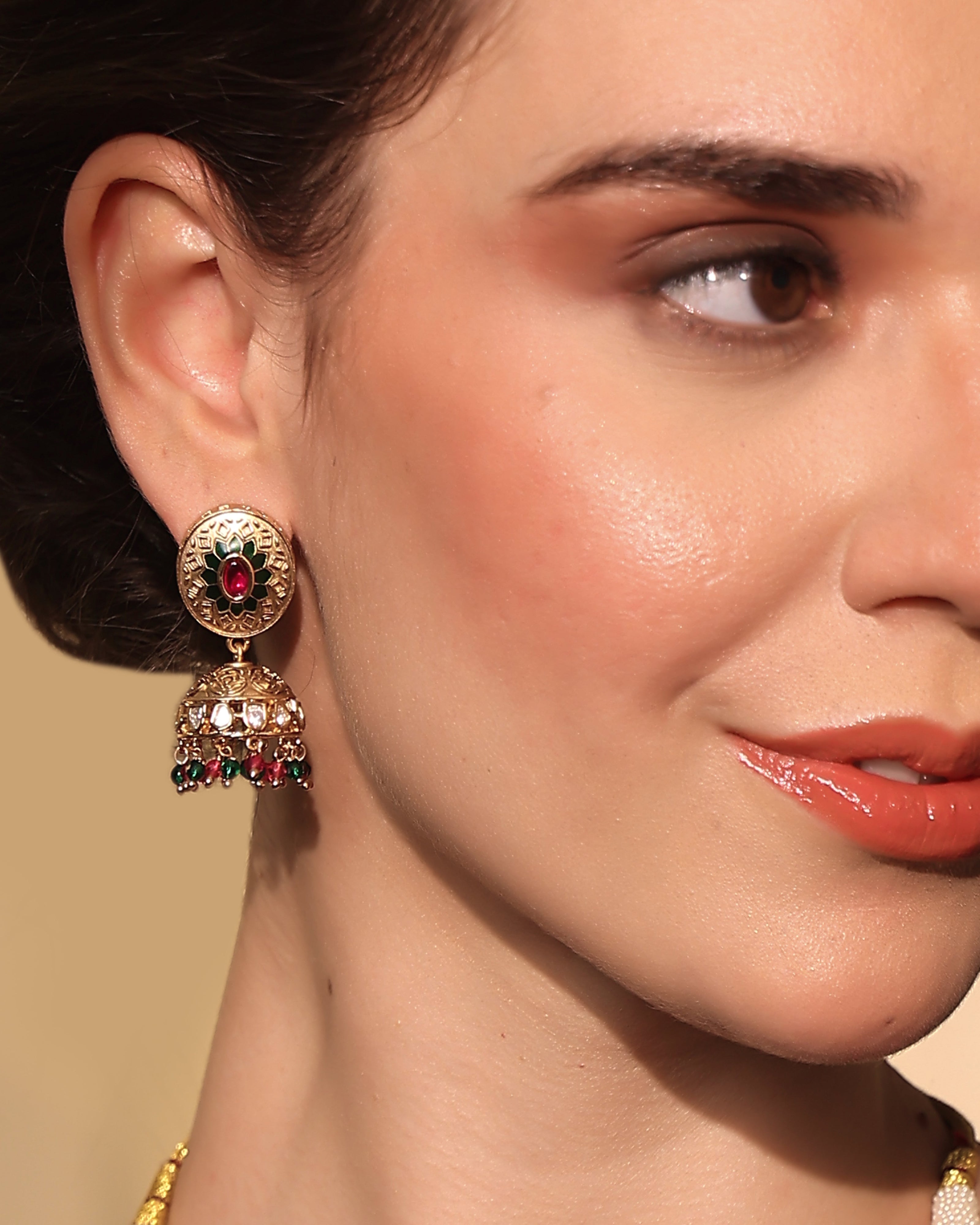 Close-up of a woman wearing gold earrings with red gemstones against a beige background