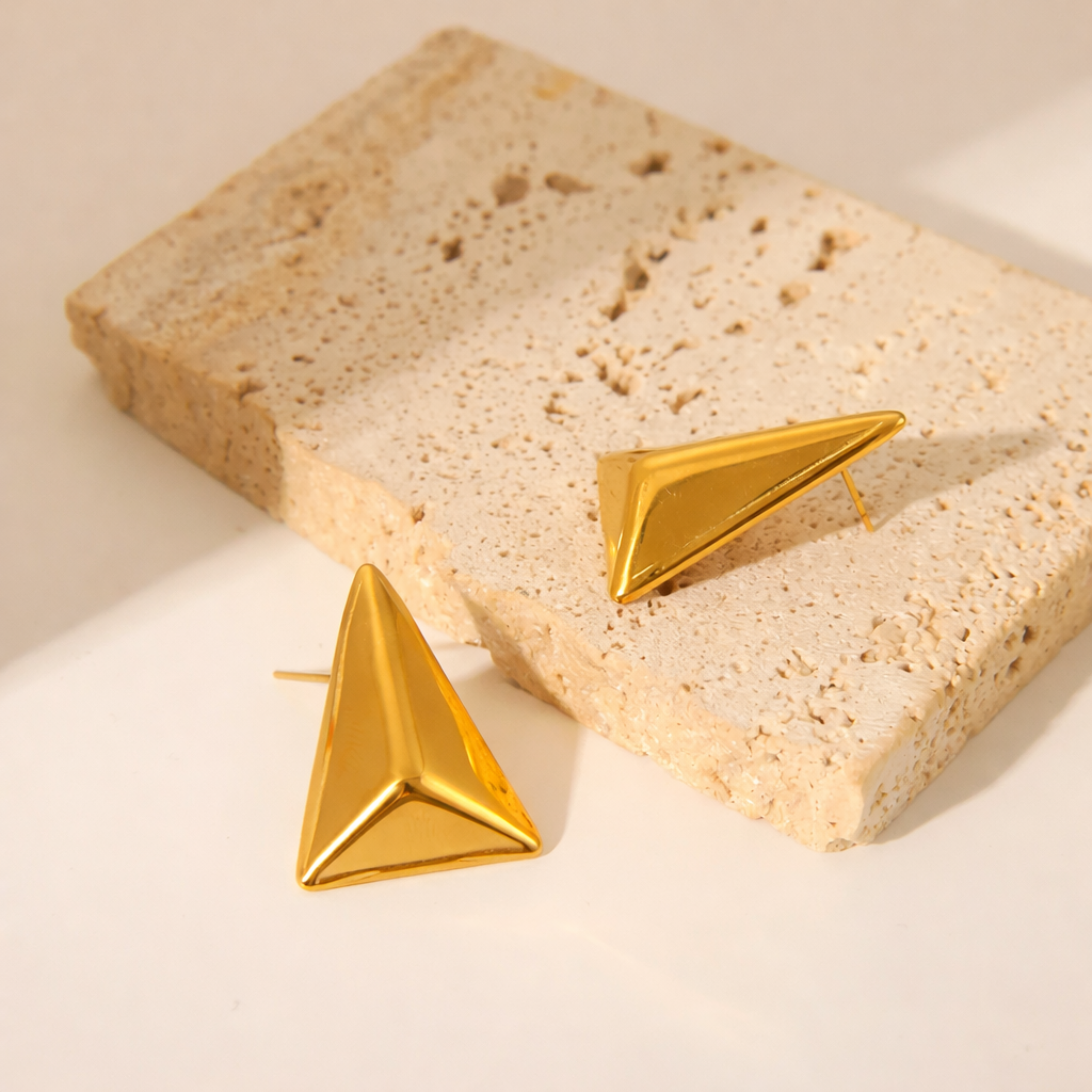 Gold triangle-shaped earrings on a textured beige surface