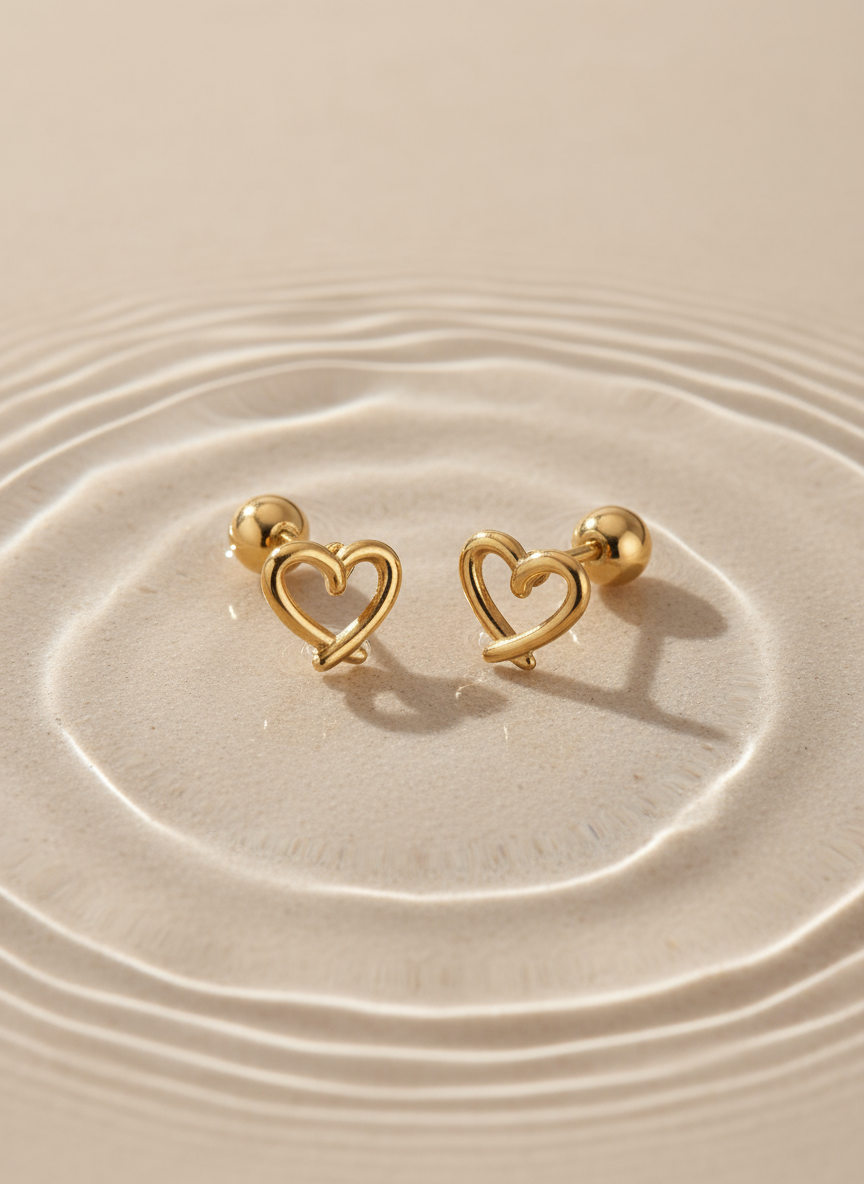 Gold heart-shaped earrings on a beige surface with water ripples